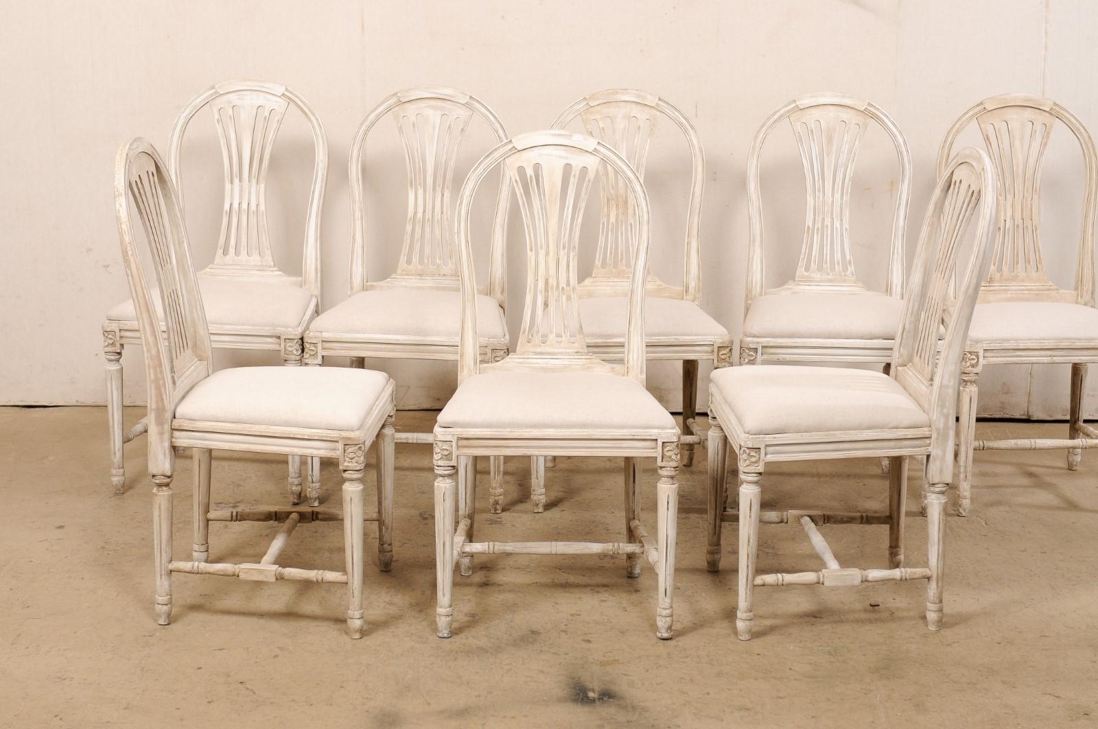 A Swedish Gustavian-style set of eight armchairs, with newly upholstered seats, from the mid 20th century. These mid-century chairs from Sweden each feature nicely curved top rails with pierced-splat backs (which take the form of the wheat-style
