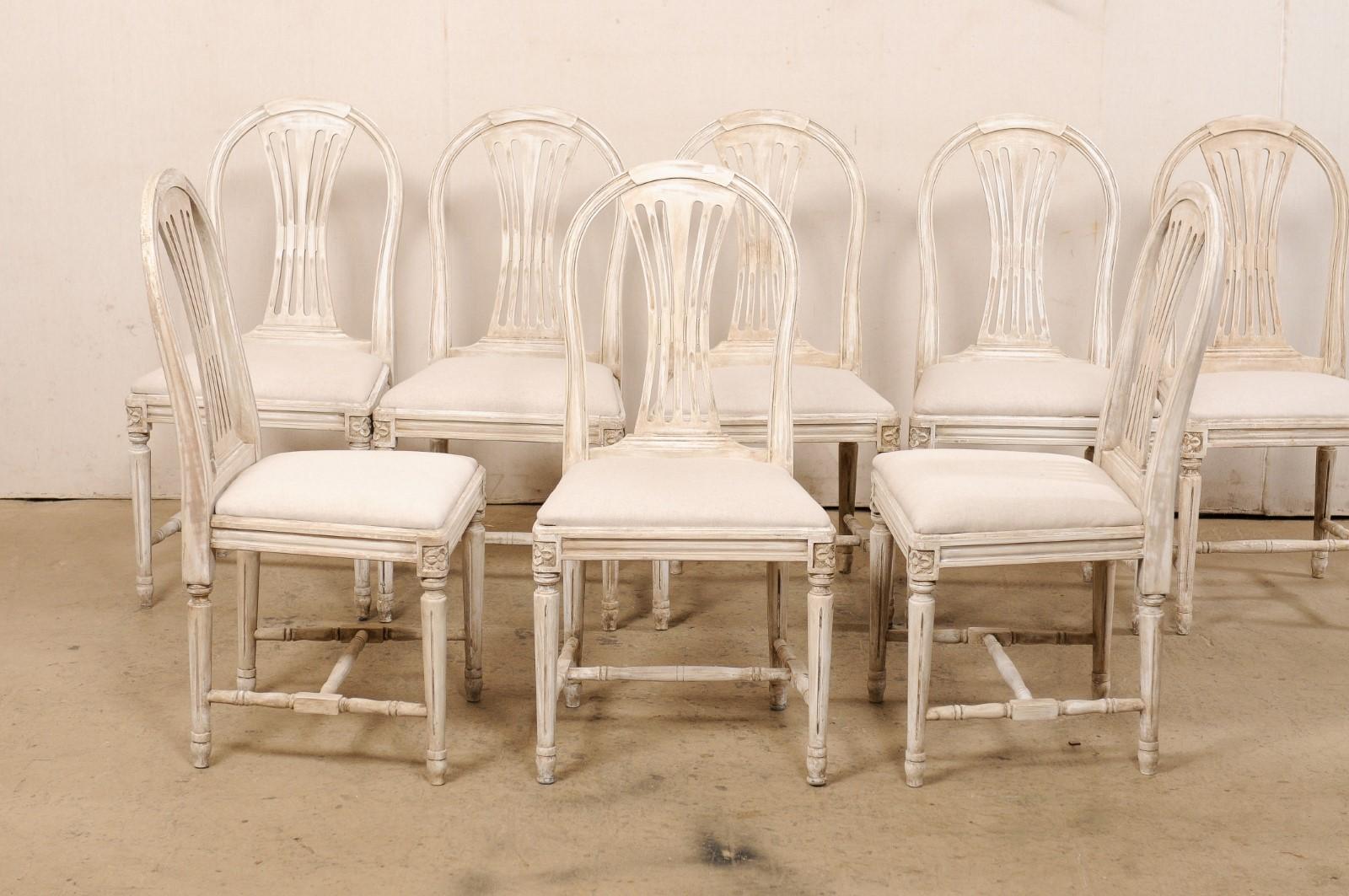 A Swedish Gustavian-style set of eight side chairs, with newly upholstered seats, from the mid 20th century. These mid-century chairs from Sweden each feature nicely curved top rails with pierced-splat backs (which take the form of the wheat-style