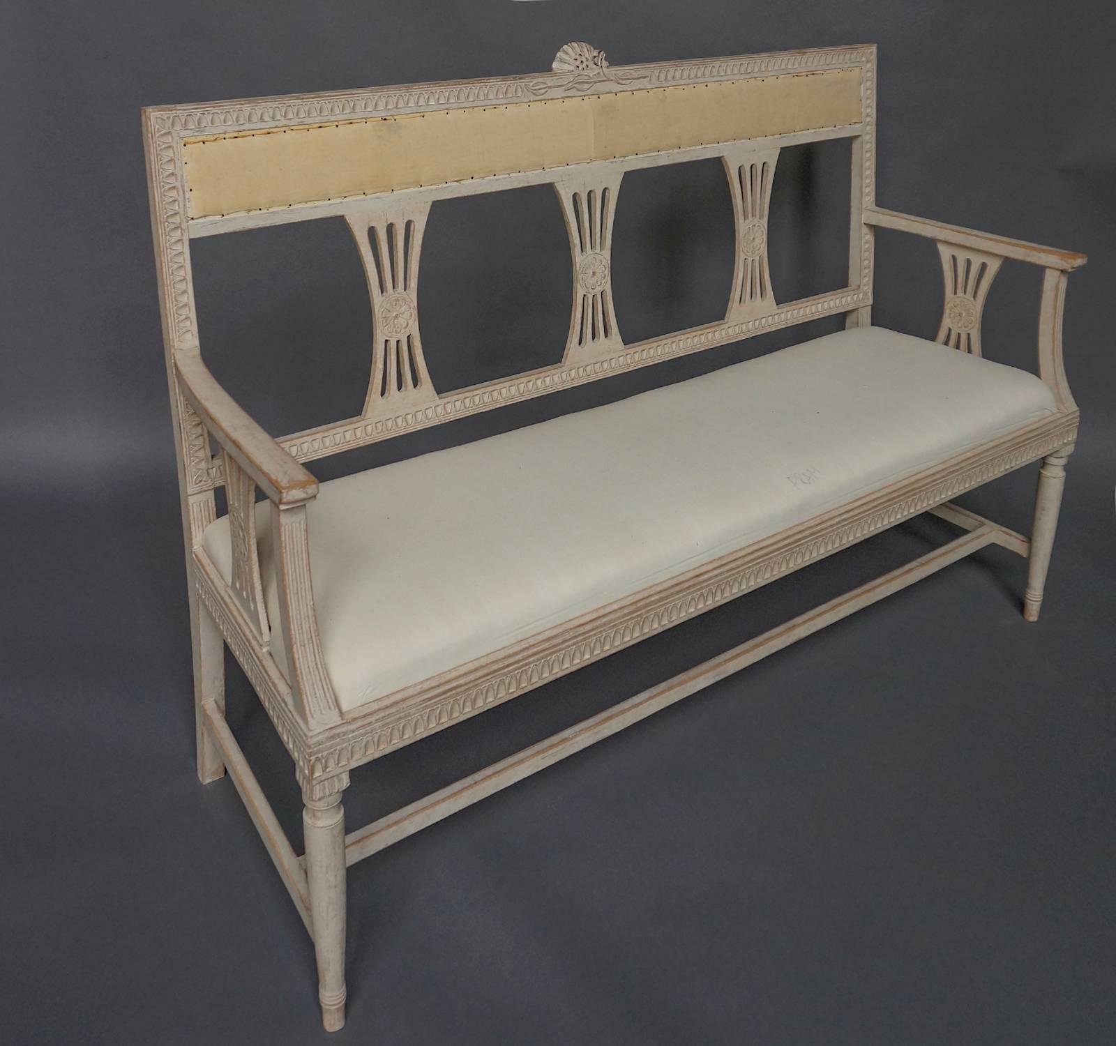Small Gustavian style settee, Sweden, circa 1910 with upholstered seat and back rest. Lambs tongue molding surrounds the back and seat, and pierced splats with central rosettes support the back and arms. A carved spray of flowers is placed at the