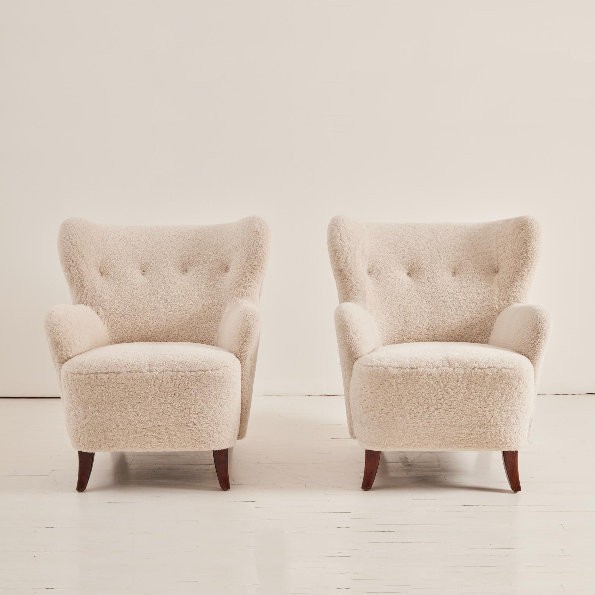 Newly upholstered Swedish Armchairs in a classic and timeless shape. Sheepskin is a soft, bone colored skin from New Zealand. Comfortable and inviting with tufted button on back rest and beech stained legs.