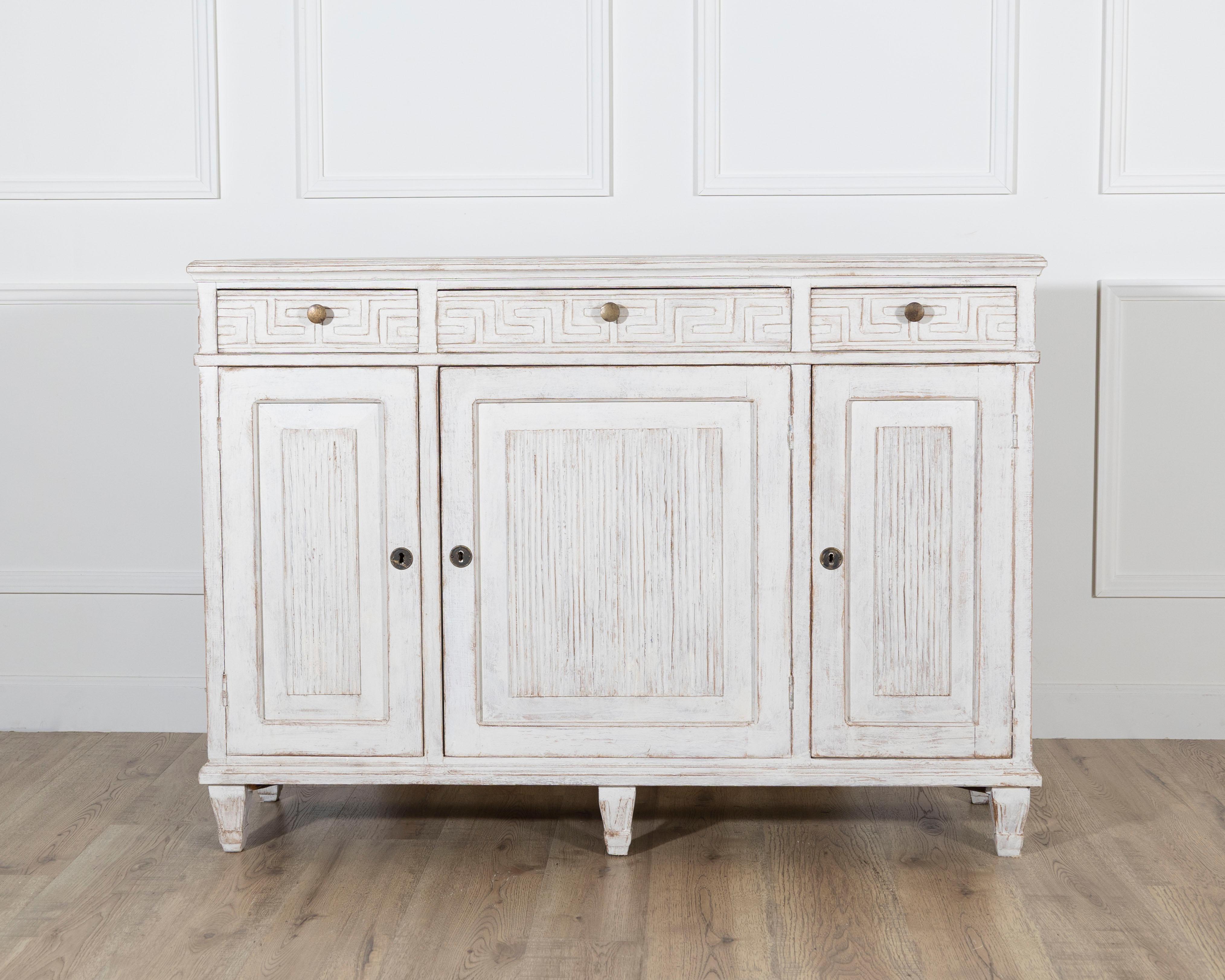 Ein hübsches schwedisches Sideboard aus der Zeit um 1880, das mit einem zarten weißen Anstrich versehen ist, der die klaren neoklassizistischen Linien und die subtilen Schnitzereien betont. Der obere Fries ist mit einem eingeschnittenen griechischen