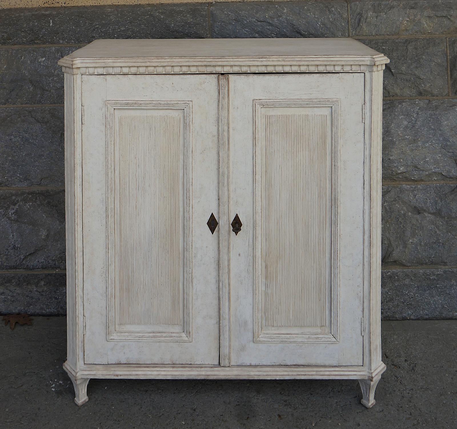 Gustavian style sideboard, Sweden, circa 1850, having a shaped top with dentil molding over double doors with fluted panels, the canted corner posts are supported by tapering square legs and decorated with incised detail. The interior has two fixed