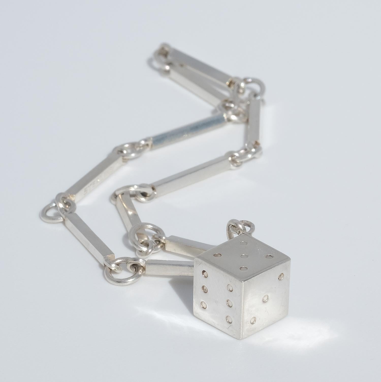 This sterling silver bracelet has a ring and bar chain, which is adorned with a silver charm in the shape of a dice. 

This bracelet fits well in both an everyday environment as well as in a more festive one and it is what we would call an everyday