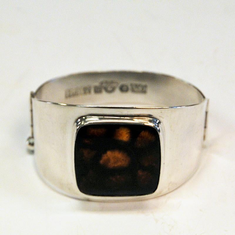 A lovely silver arm bracelet by Hans J Weissenberg Konsthandtverk, Björklinge Sweden 1963. Beautiful and easy to wear vintage bracelet with a beautiful square shaped shimmering glass stone with black and golden browns patterns. Open entrance with a