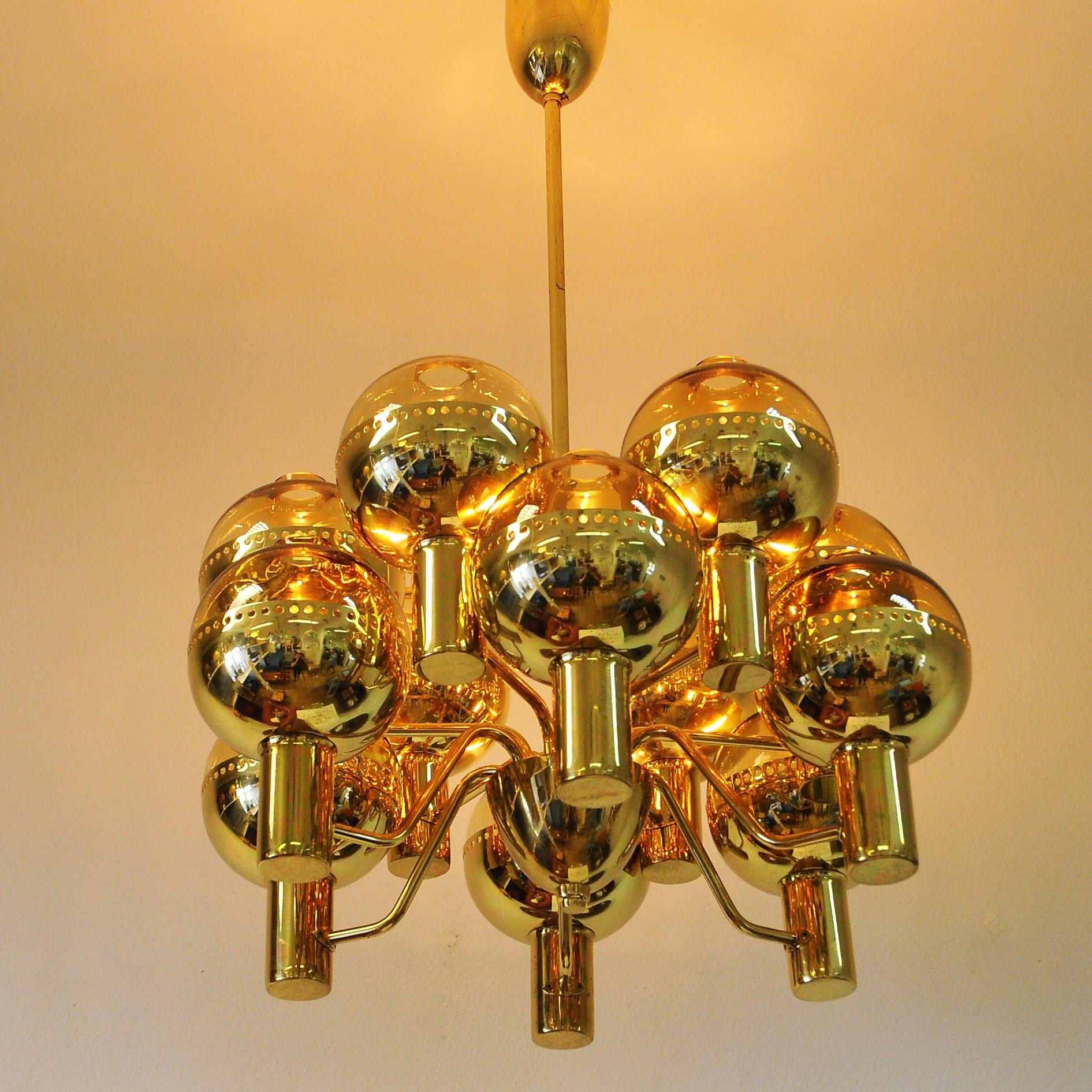 A beautiful and stunning special edition Patricia chandelier model T372/12 by Hans-Agne Jakobsson. Twelve-armed chandelier made in polished brass and gold colored glassdomes held up of golden cup. The cups have small round holes around the boarder.