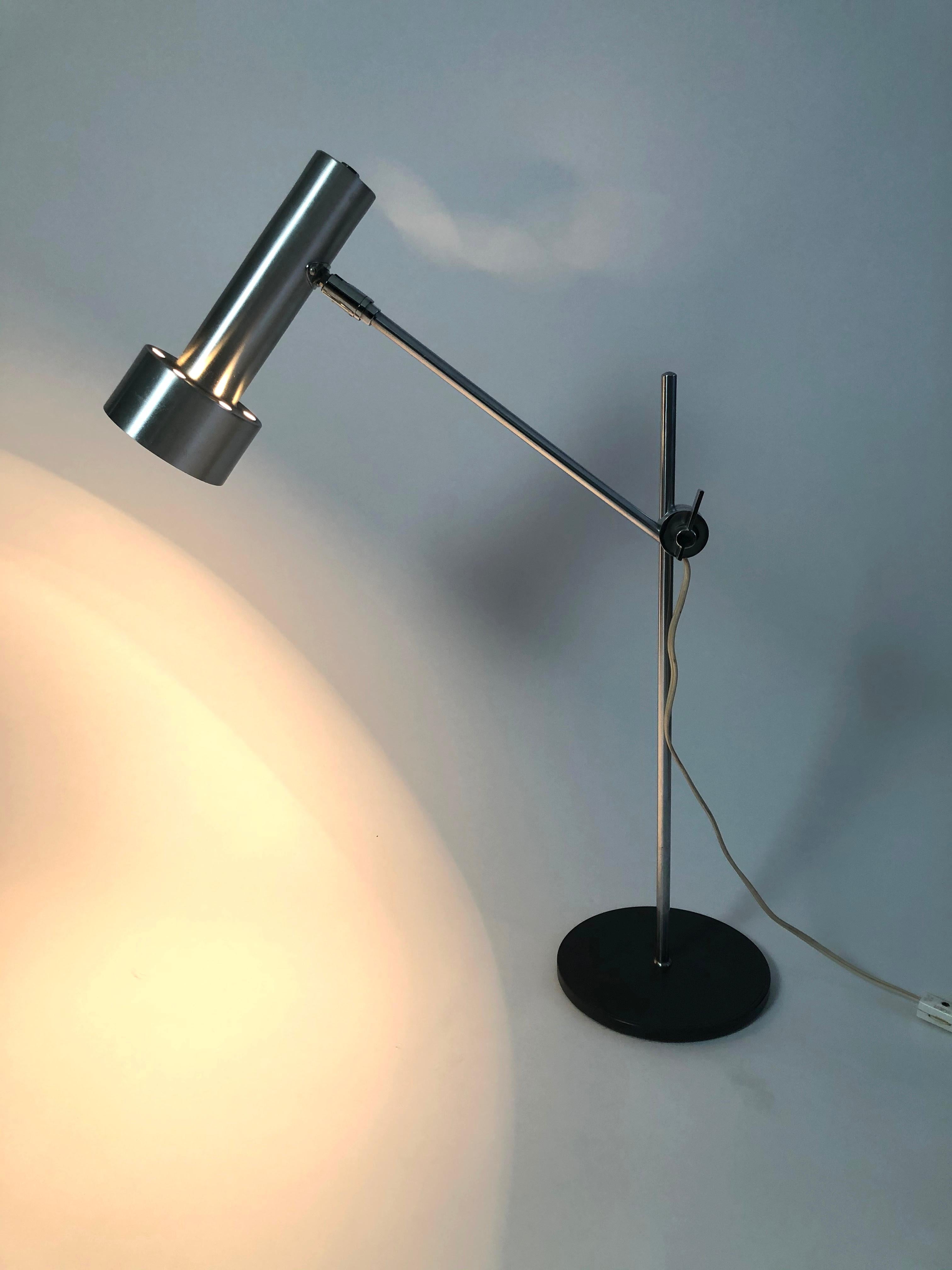 A Swedish adjustable height desk lamp, with cylindrical brushed steel shade on a chromed metal post with circular black metal base. The shade can be moved up and down the post to the desired height and the shade can be easily angled to a wide range