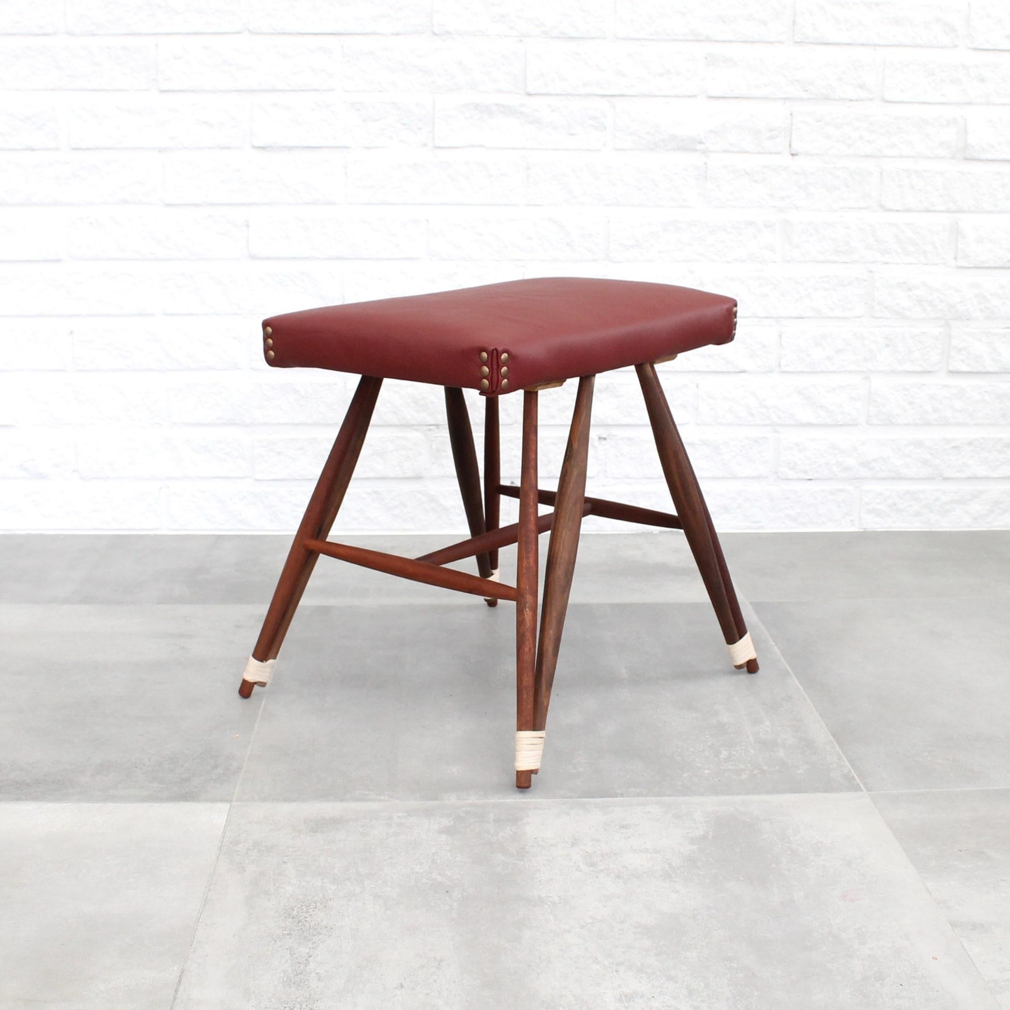 This unique Swedish stool features a solid walnut construction, complemented by red leather upholstery and distinctive rattan details around the legs. Notably, its characteristic Eiffel silhouette is achieved through the use of two wooden dowels for