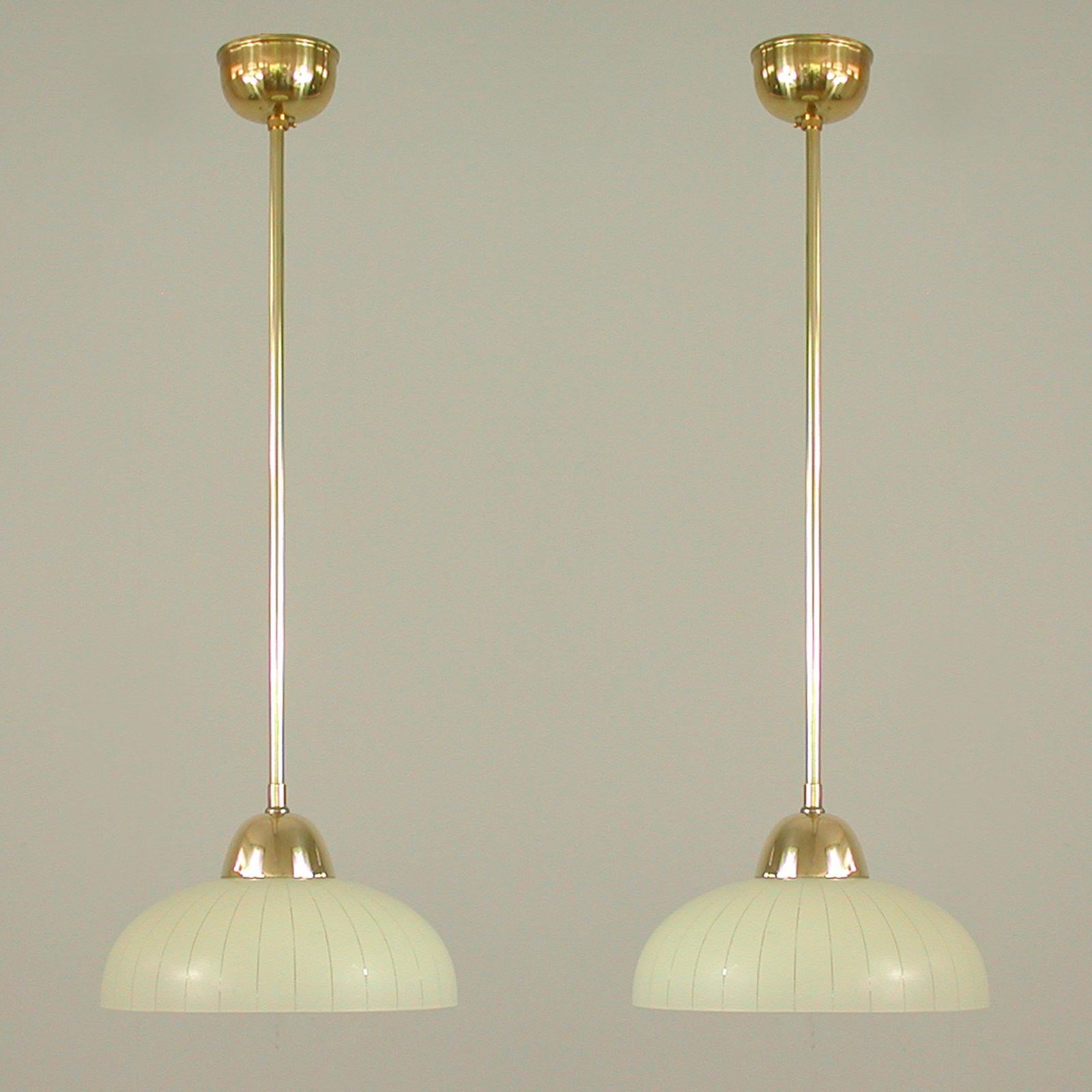 These elegant minimalist pendants were designed and manufactured in Sweden in the 1940s to 1950s. 

The lights feature a round cream colored striped glass lampshade and brass hardware. They requires one E27 bulb and have been rewired for use in US