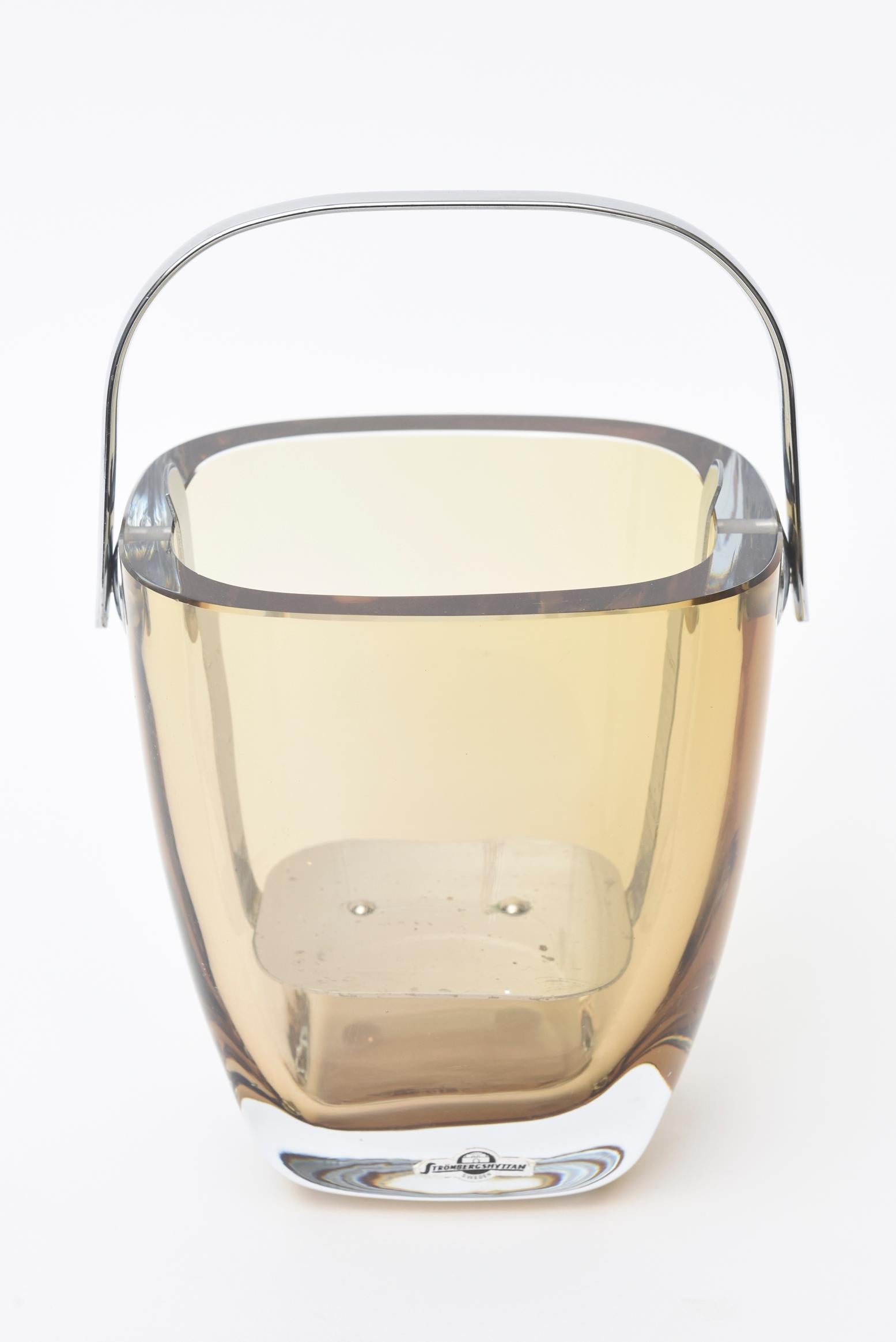 This lovely Scandinavian Modern hallmarked Strombergshyttan small vintage ice bucket is transparent amber tinted glass with a modern chrome handle. It has the original ice stand inside. The top is flat cut pulsed glass and is from the 1960s. The