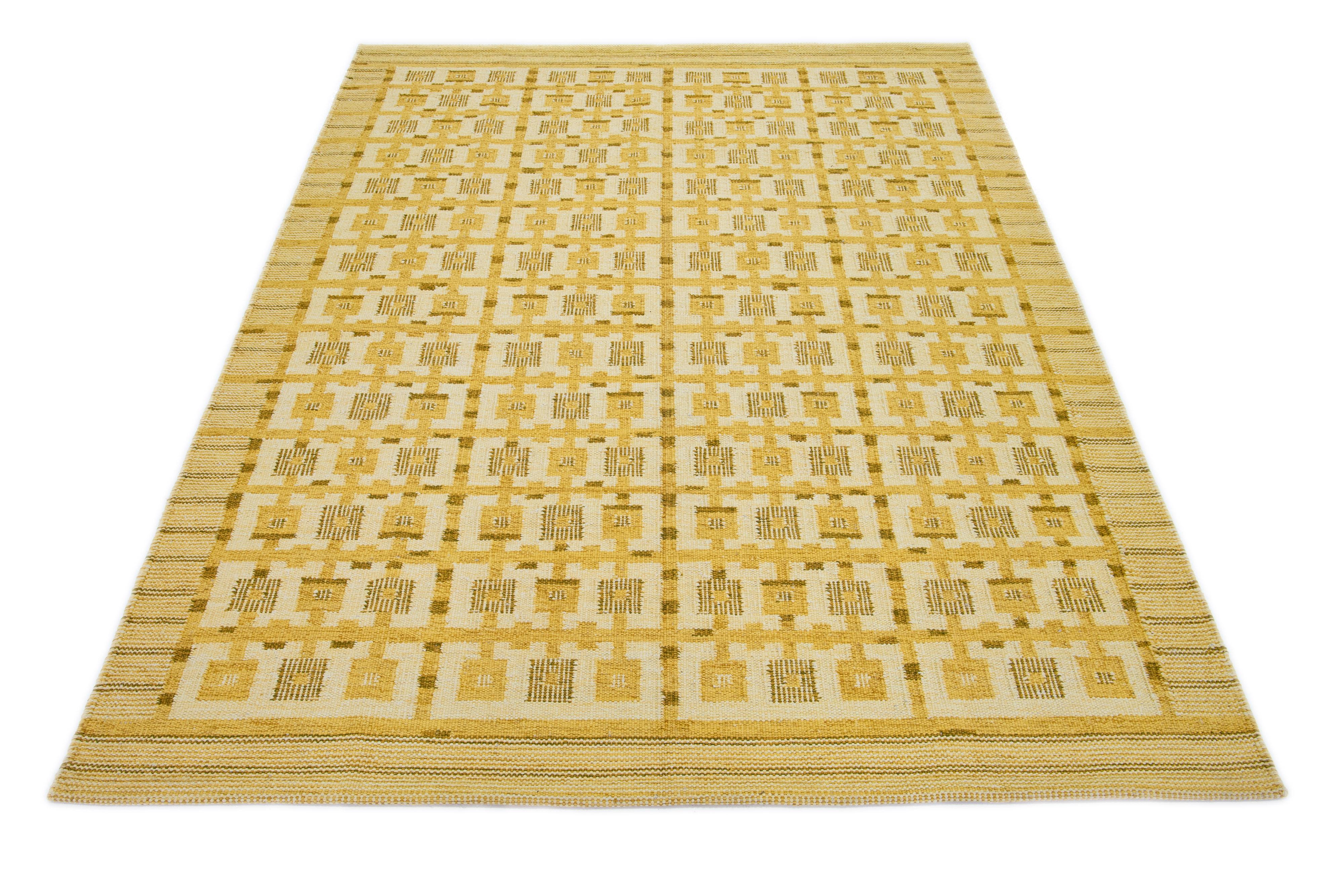 Dieser Flachgewebe-Teppich zeigt ein schickes, modernes schwedisches Design mit gelber Feldfarbe. Der Teppich ist mit einem geometrischen Muster in Beigetönen versehen.

 Dieser Teppich misst 7'11
