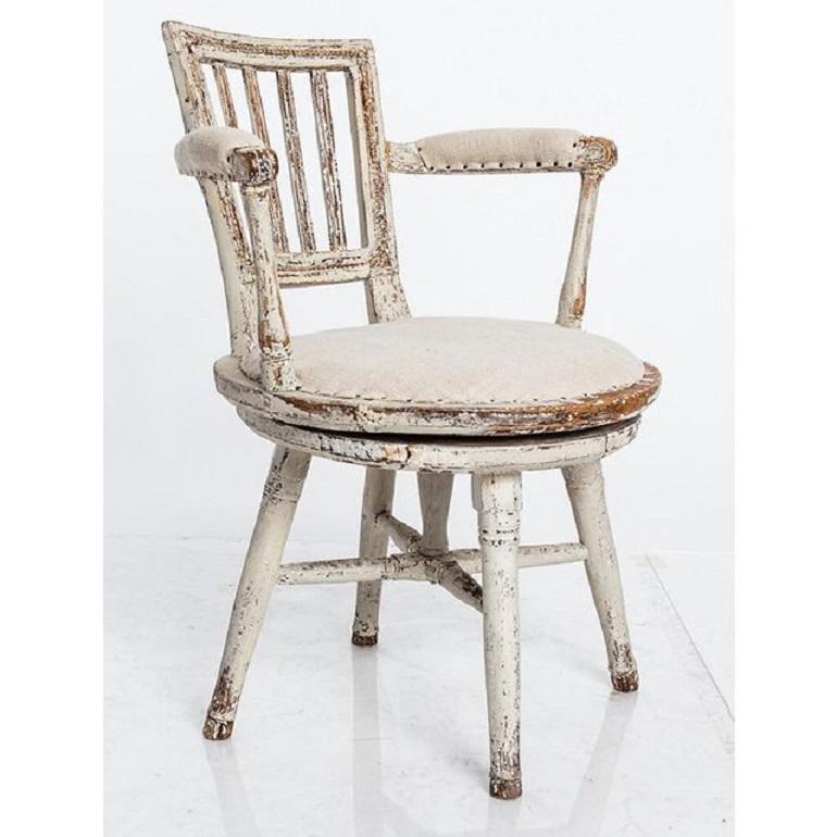 The antique Swedish Gustavian style swivel chair with historic white paint is a chair that was made in Sweden circa 1830s. The chair has a working swivel mechanism that allows it to rotate. The white paint finish has aged over time, giving it an