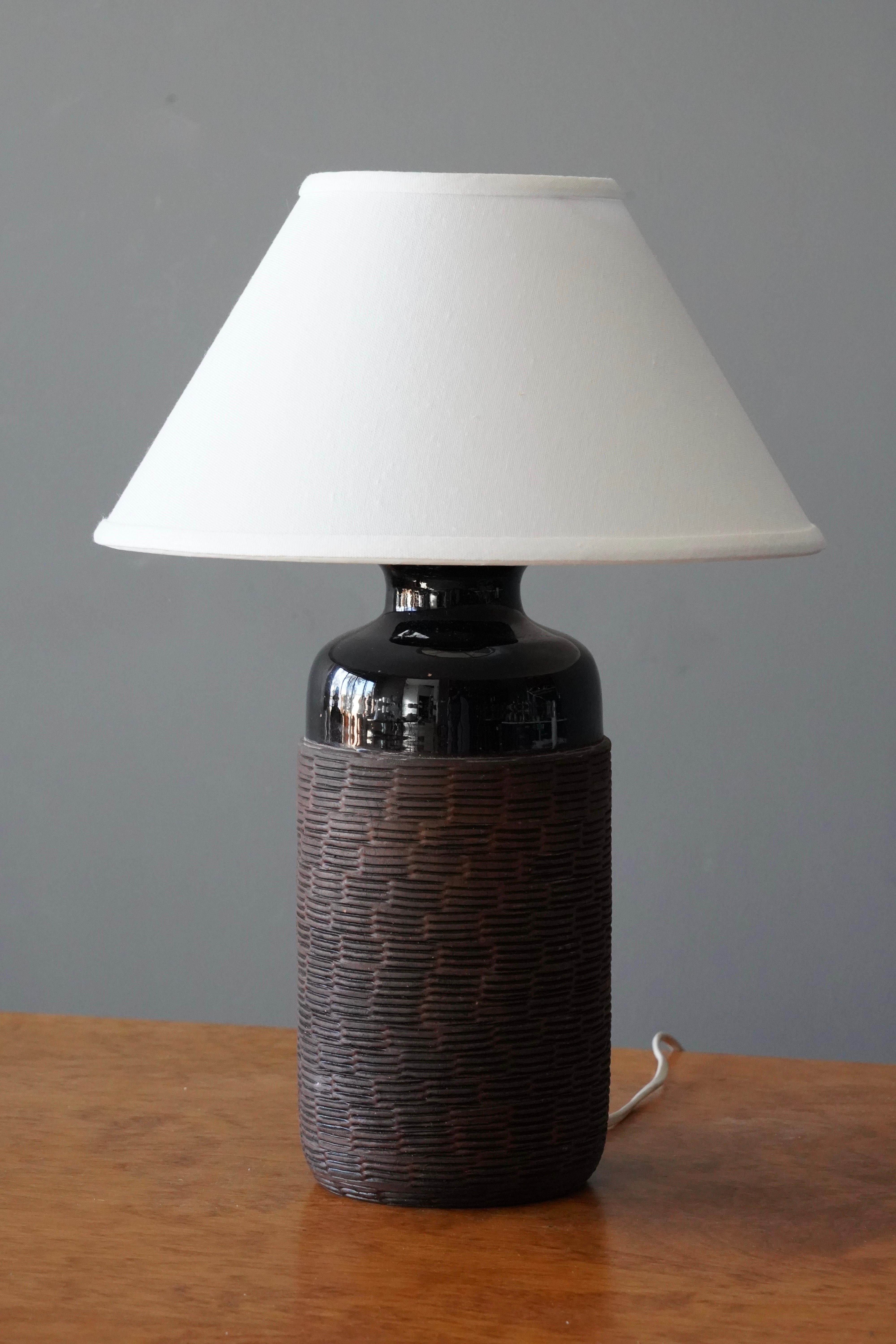 A table lamp, designed and produced in Sweden, c. 1960s. Likely studio production. Features high gloss black glaze and unglazed brown stoneware with simple incised decoration.

Dimensions listed are without shade. 
Dimensions with shade: Height