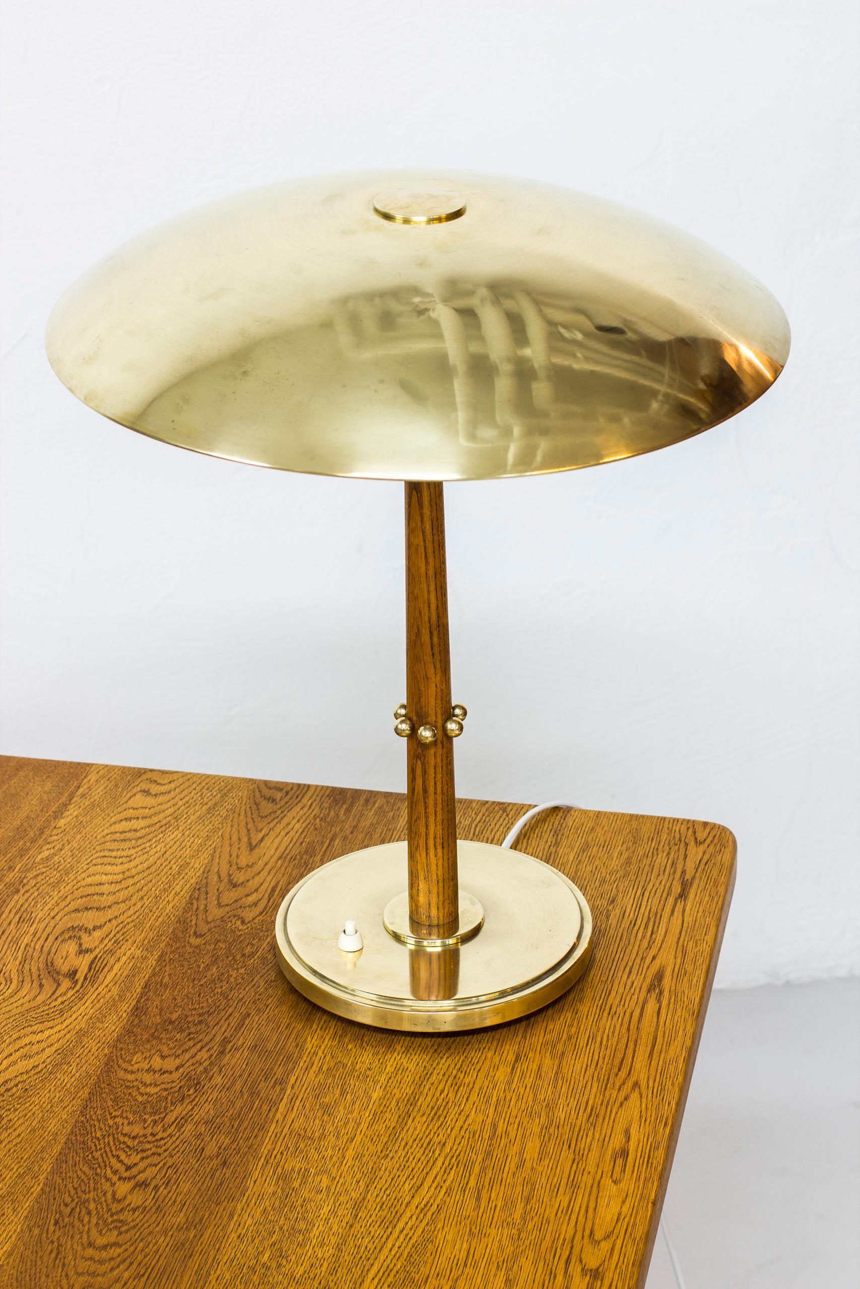Table lamp designed by Harald Notini. Produced in Stockholm, Sweden by Böhlmarks during the 1940s. Made from solid polished brass with a stem of solid oak. Light switch on the base in working order. Good vintage condition with age related wear and