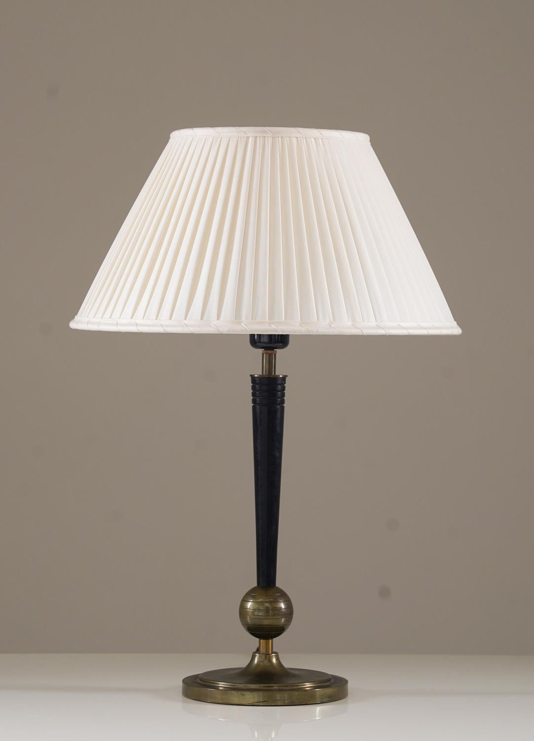 Elegant table lamp, crafted by Böhlmarks in the 1930s. The design features a sleek, tapered stem anchored by a spherical brass detail and a solid, circular base. The lamp is complemented by a newly custom-made pleated lampshade, created from vintage