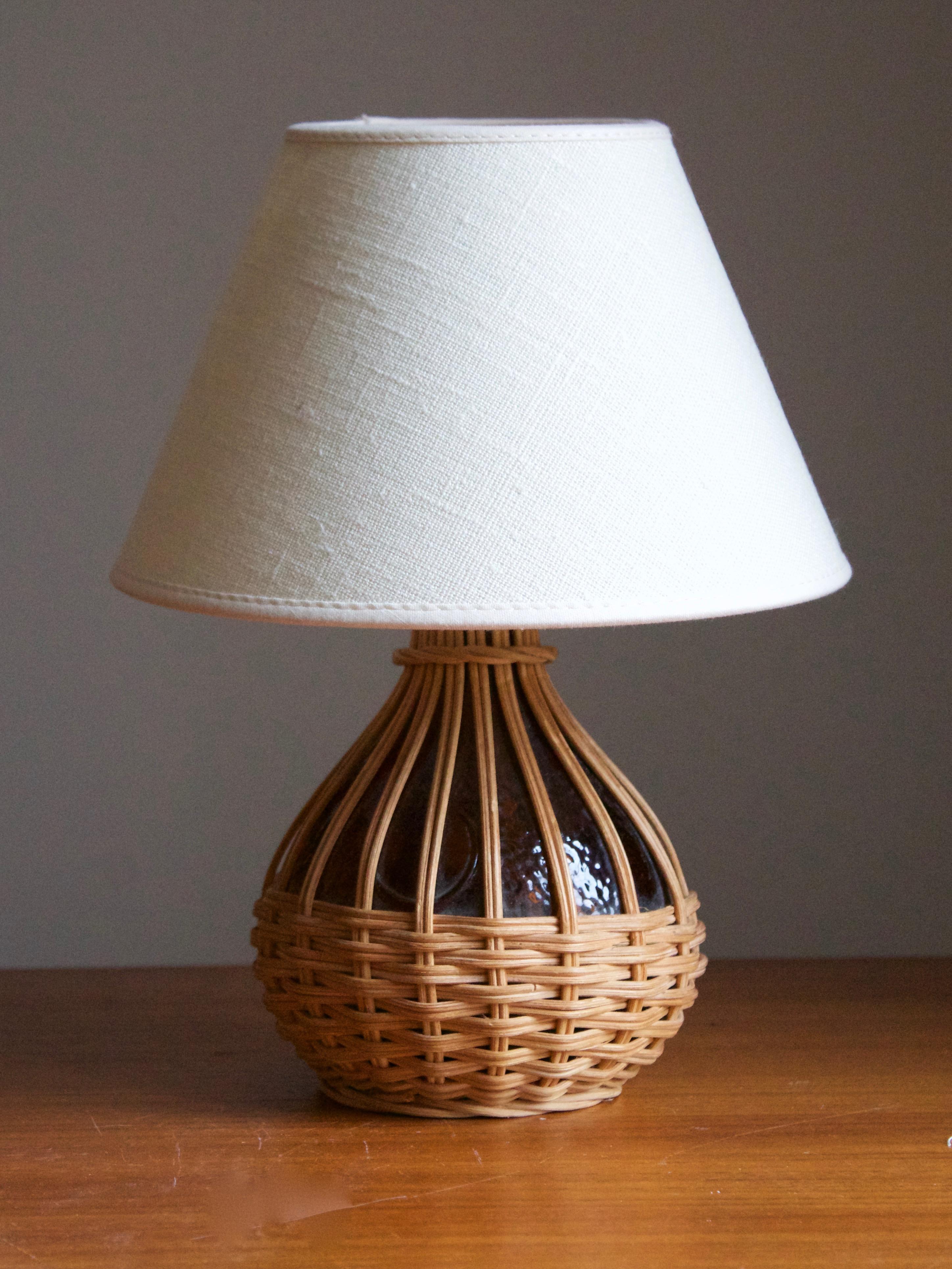 A table lamp, designed and produced in Sweden, c. 1970s.

Red-stained glass wrapped in rattan. 

Stated dimensions exclude lampshade. Height includes socket. Sold without lampshade.