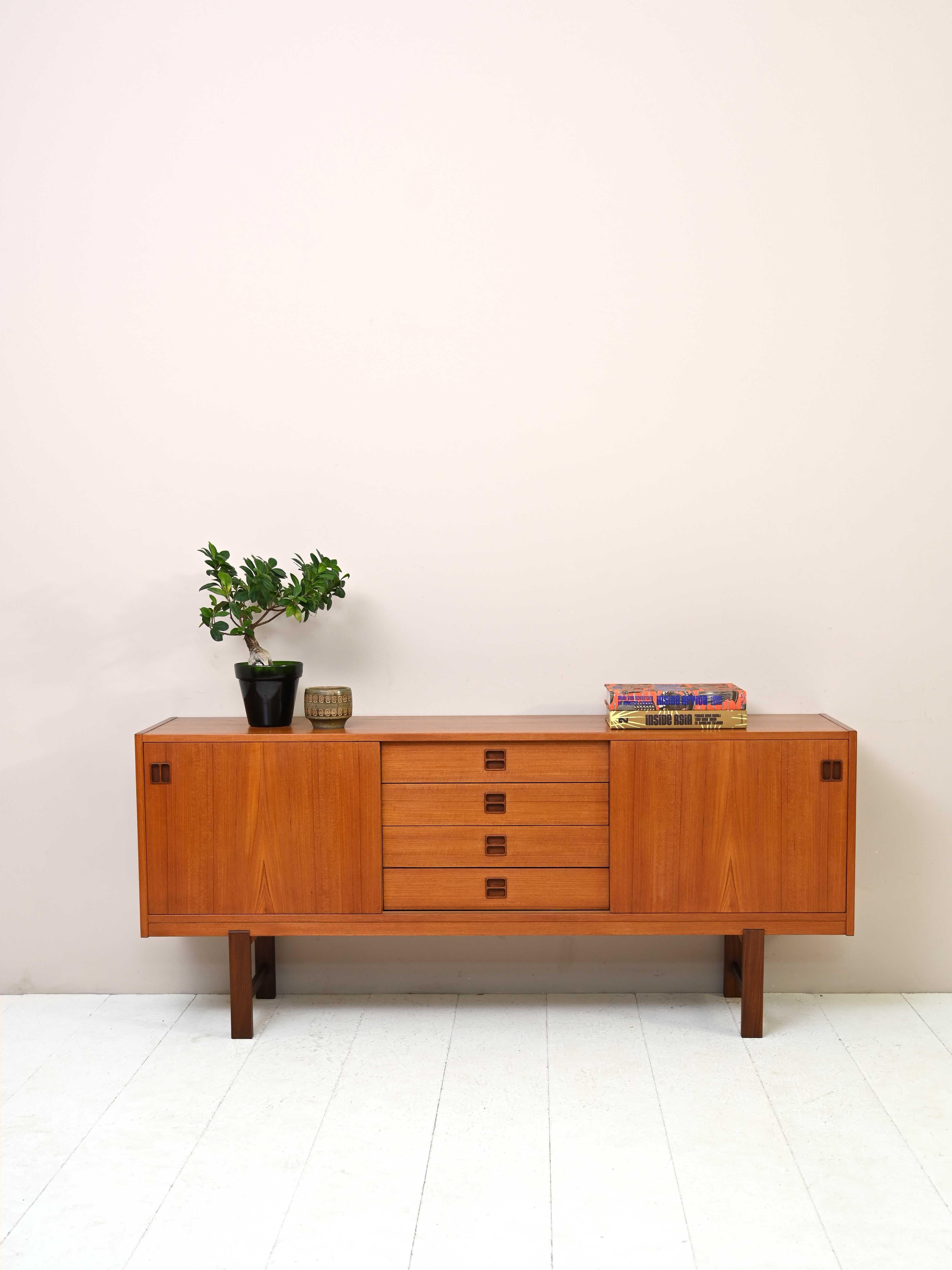Vintage 1960s teak sideboard.
 
This classic and elegant piece of furniture features two compartments on the sides with sliding doors and 4 central drawers. The carved wooden handle gives it a unique and distinctive look.
She squared Teak wood