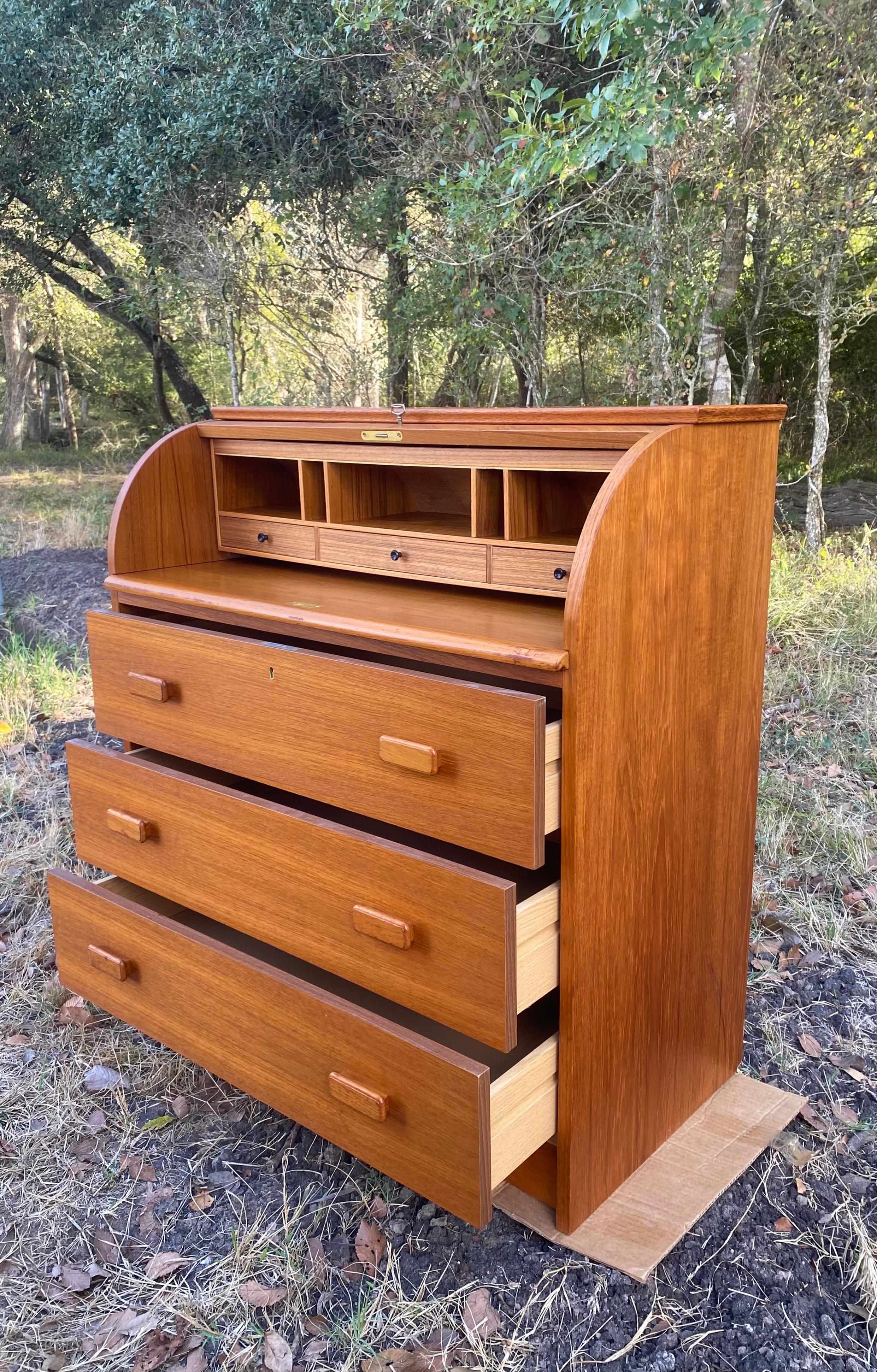 Streamlined teak writing bureau / desk designed by Egon Ostergaard. Cubbies and three small drawer compartments are hidden behind a locking roll top. A sliding desk surface tucks away and can be fully concealed or extended out for more writing or