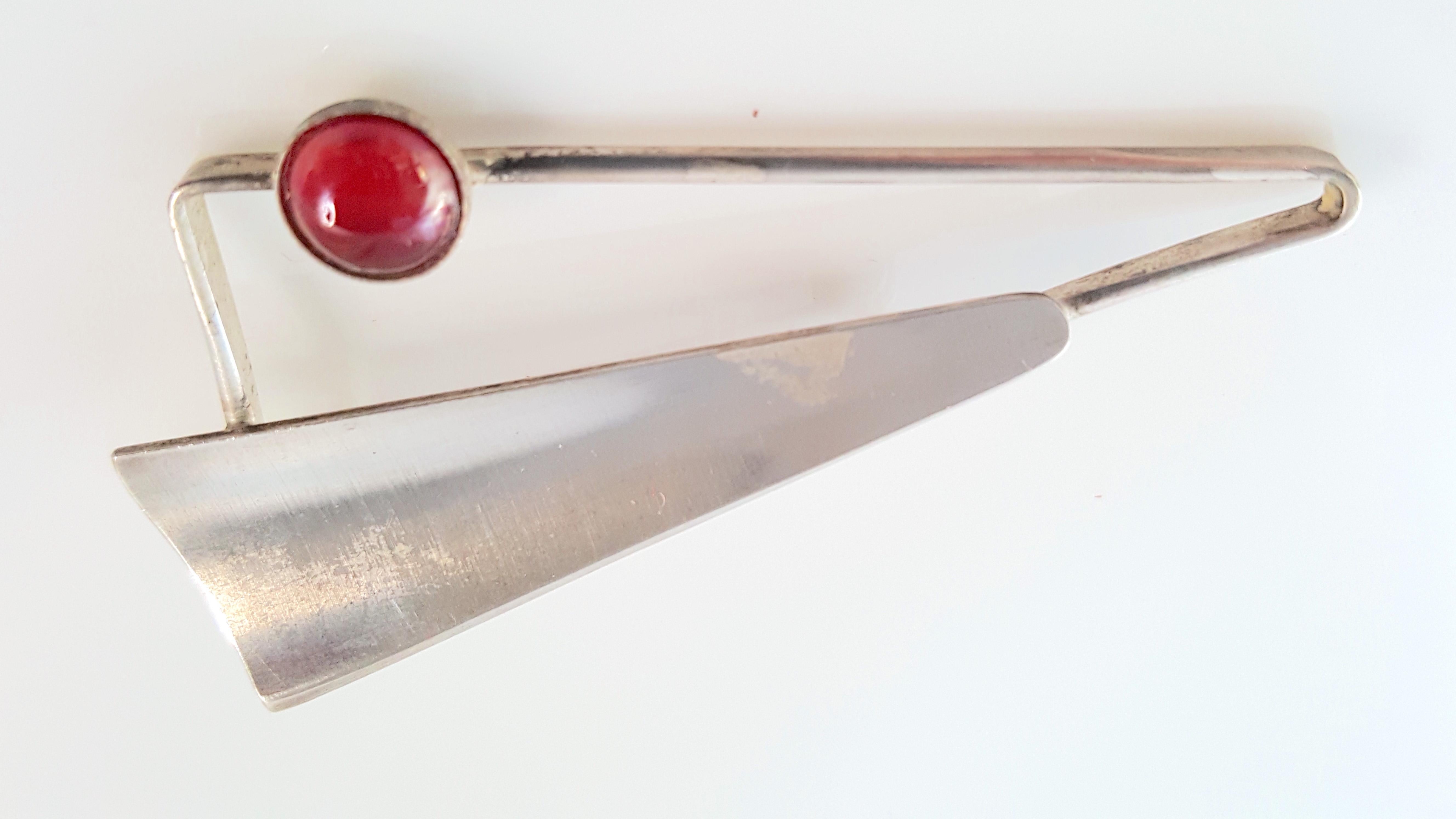 Made in 1962 by Swedish Rune Tennesmed, this modern minimal sterling silver geometric brooch features a faux ruby poured-glass red cabochon, concave sheet metal, and openwork that forms two corners of the two-tier triangular brooch. This simple