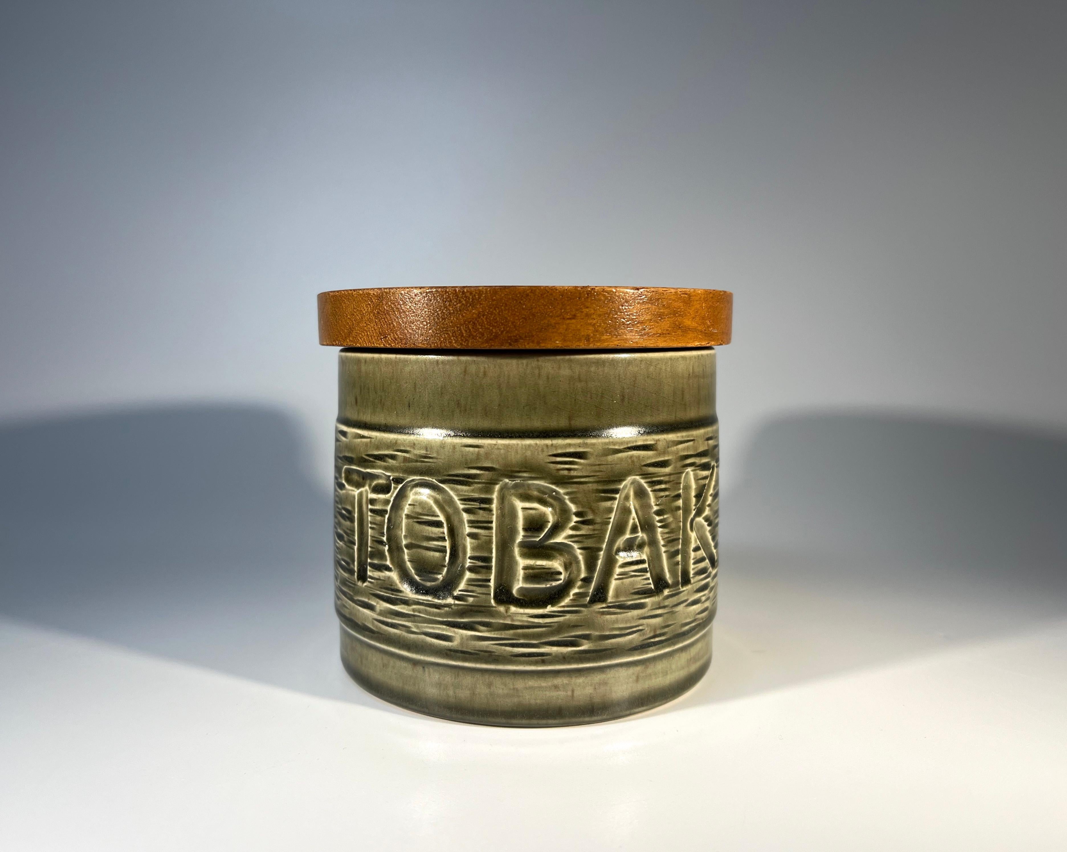 Typically Scandinavian understated and functional, ceramic tobacco jar with teak wooden lid
Tobak boldly incised within a subtle dark muted green glaze
Stamped Made in Sweden #903 on base
The tight fitting lid is fitted with cork inner
Circa