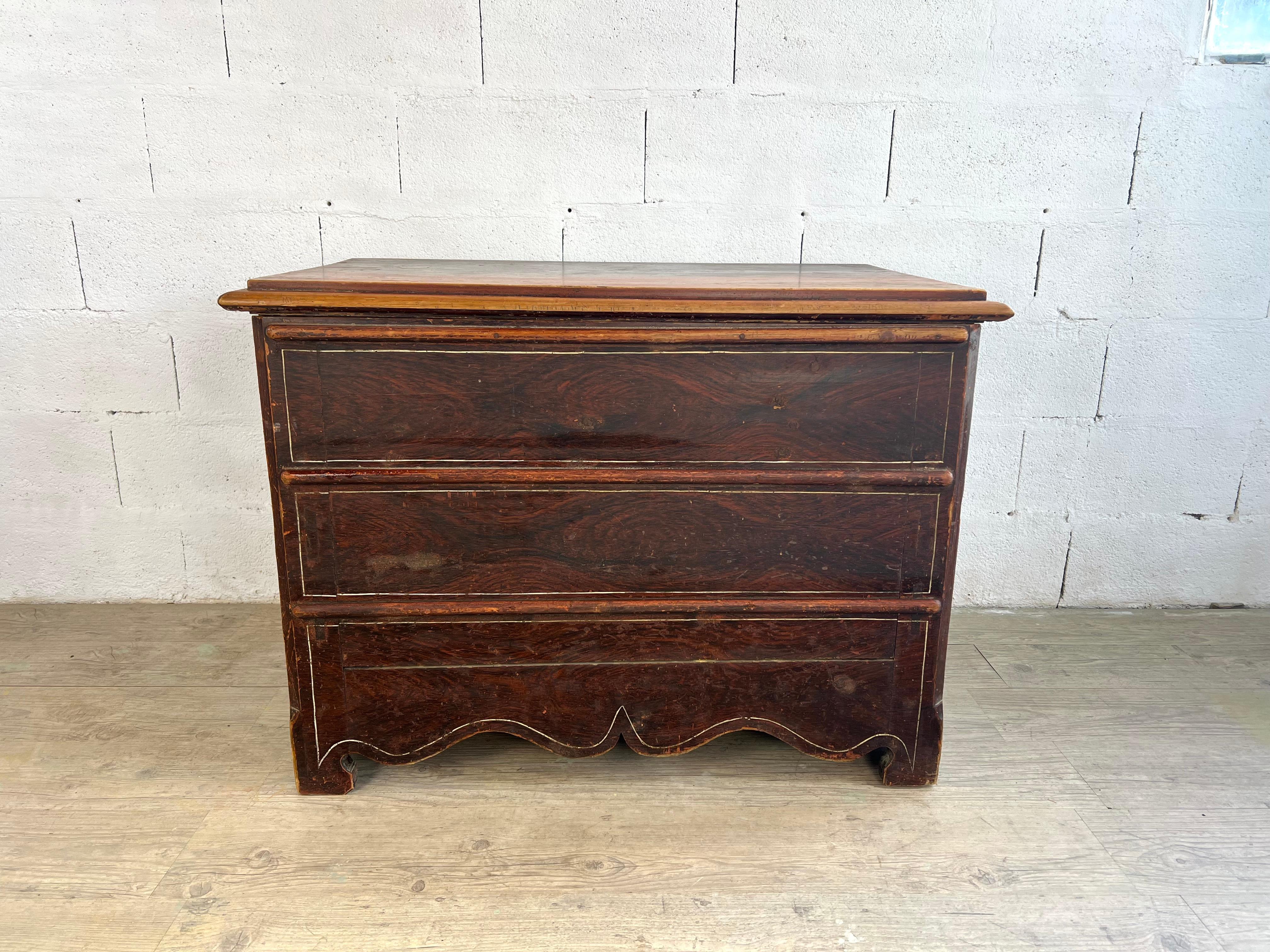 Diese charmante schwedische Trompe-l'œil-Kommode ist ein Meisterwerk an Design und Funktionalität. Mit einer Patina aus Holzimitat lackiert, ahmt es geschickt das Aussehen einer traditionellen Kommode mit drei Schubladen nach und verbirgt dabei ein