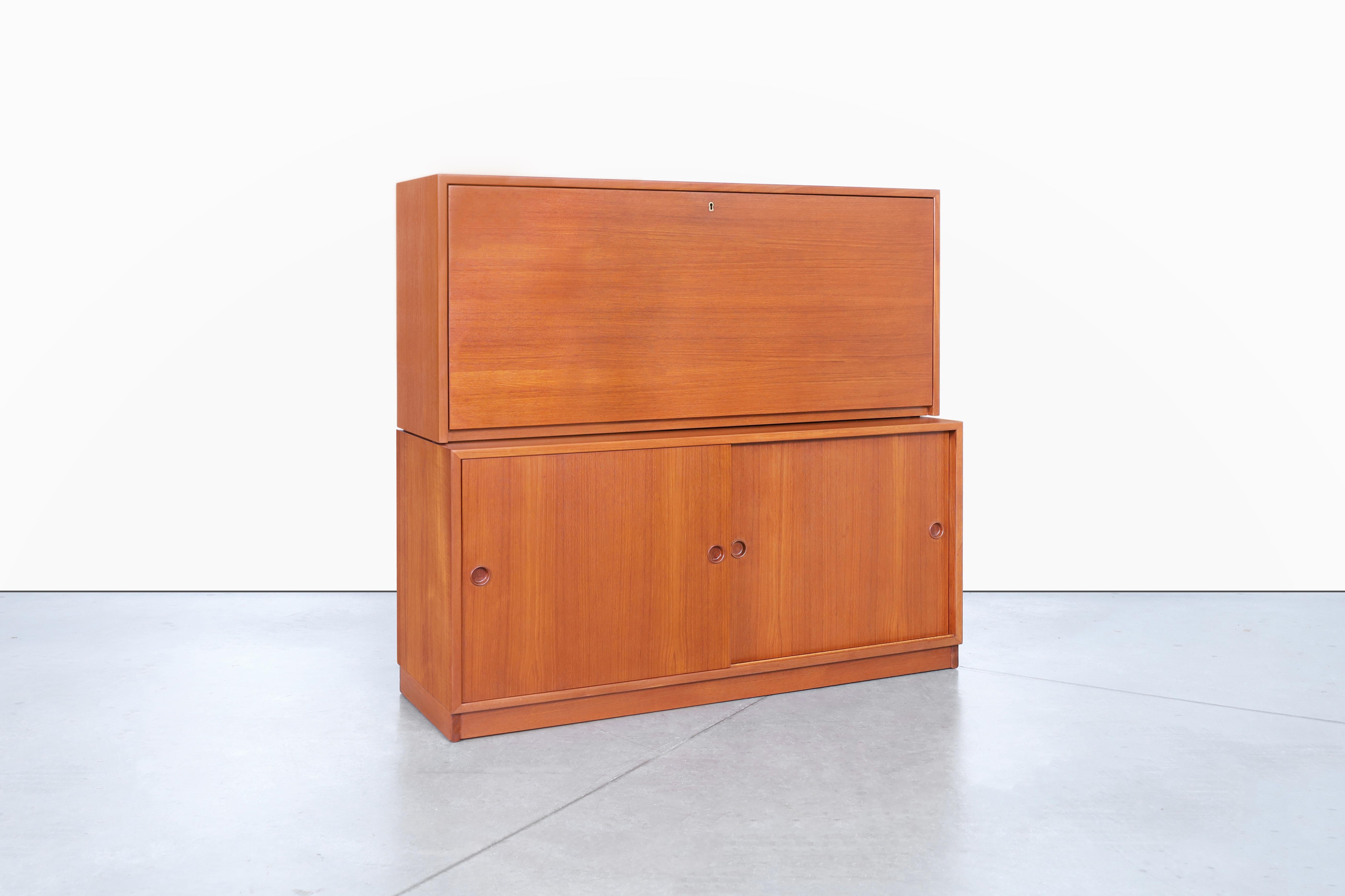 Questo mobile svedese in teak a due pezzi, disegnato da Børge Mogensen e prodotto da Karl Andersson negli anni '60, è un pezzo d'arredamento straordinario. Lo scomparto superiore è dotato di un'anta a ribalta che si trasforma in una scrivania, di
