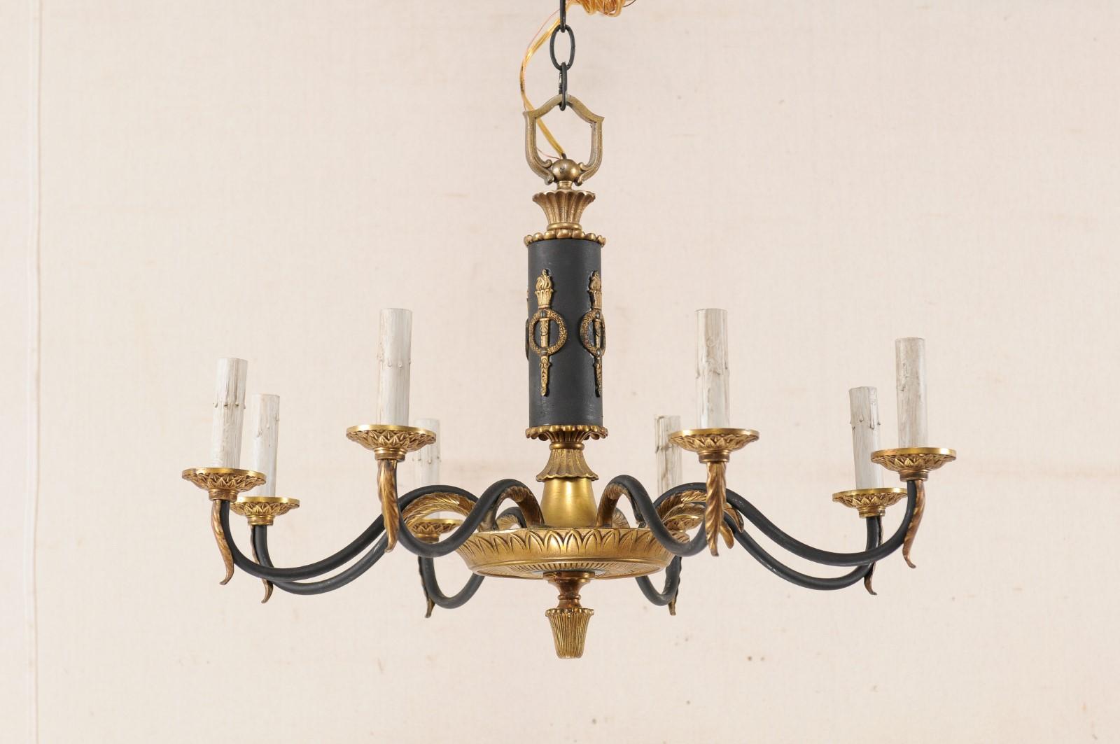 A Swedish eight-light black and gold toned neoclassical style chandelier. This vintage chandelier from Sweden features a Neoclassical design with central column adorn in wreathed torches, and larger brass gallery in ribbed finish and leaf motif with