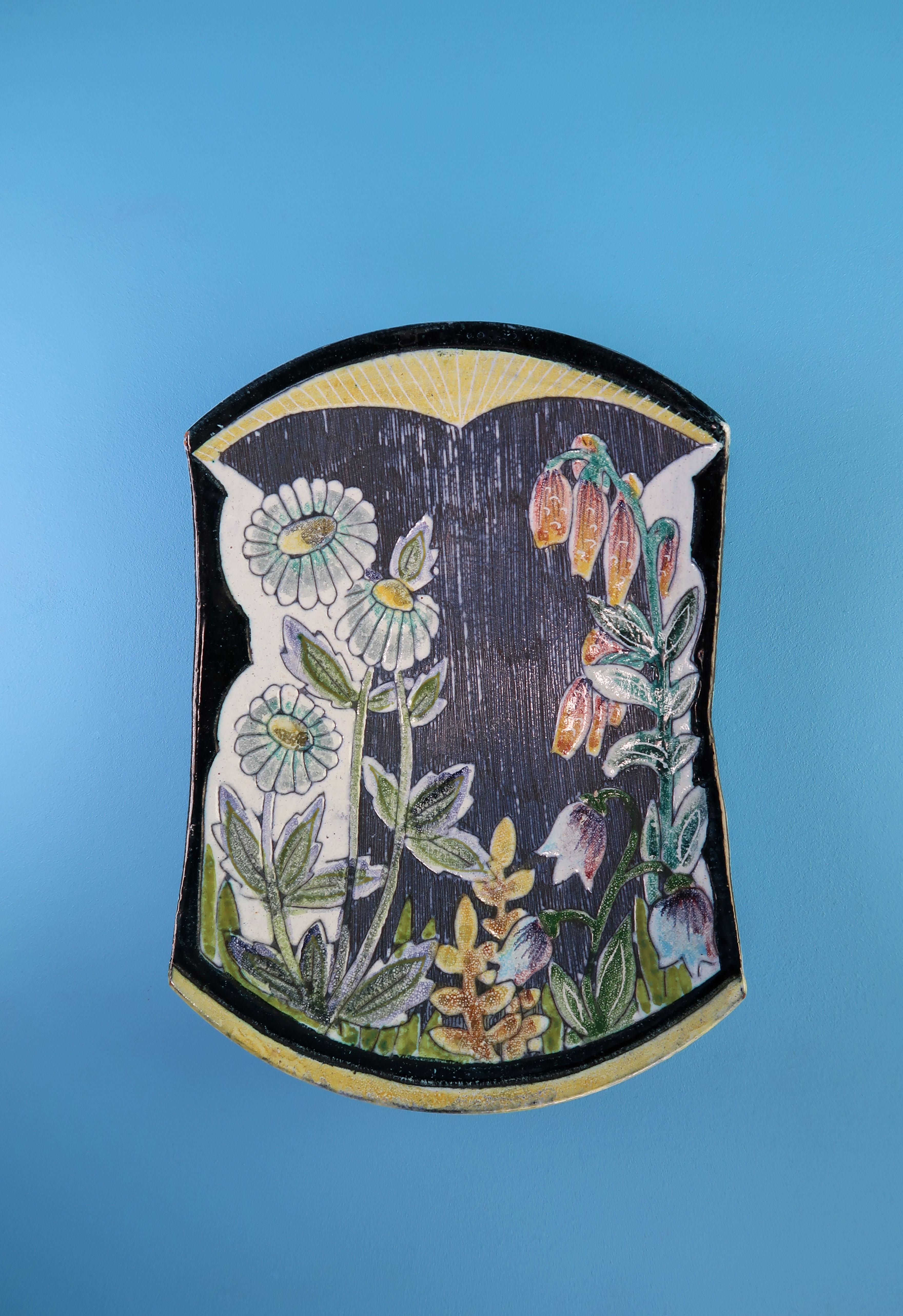 Plateau mural en céramique de style moderne du milieu du siècle, fabriqué à la main par le suédois Tilgmans en 1957. Décor floral peint à la main en couleurs blanc, jaune, orange, rose, bleu clair et vert sur base noire. Glace bleu clair et décor