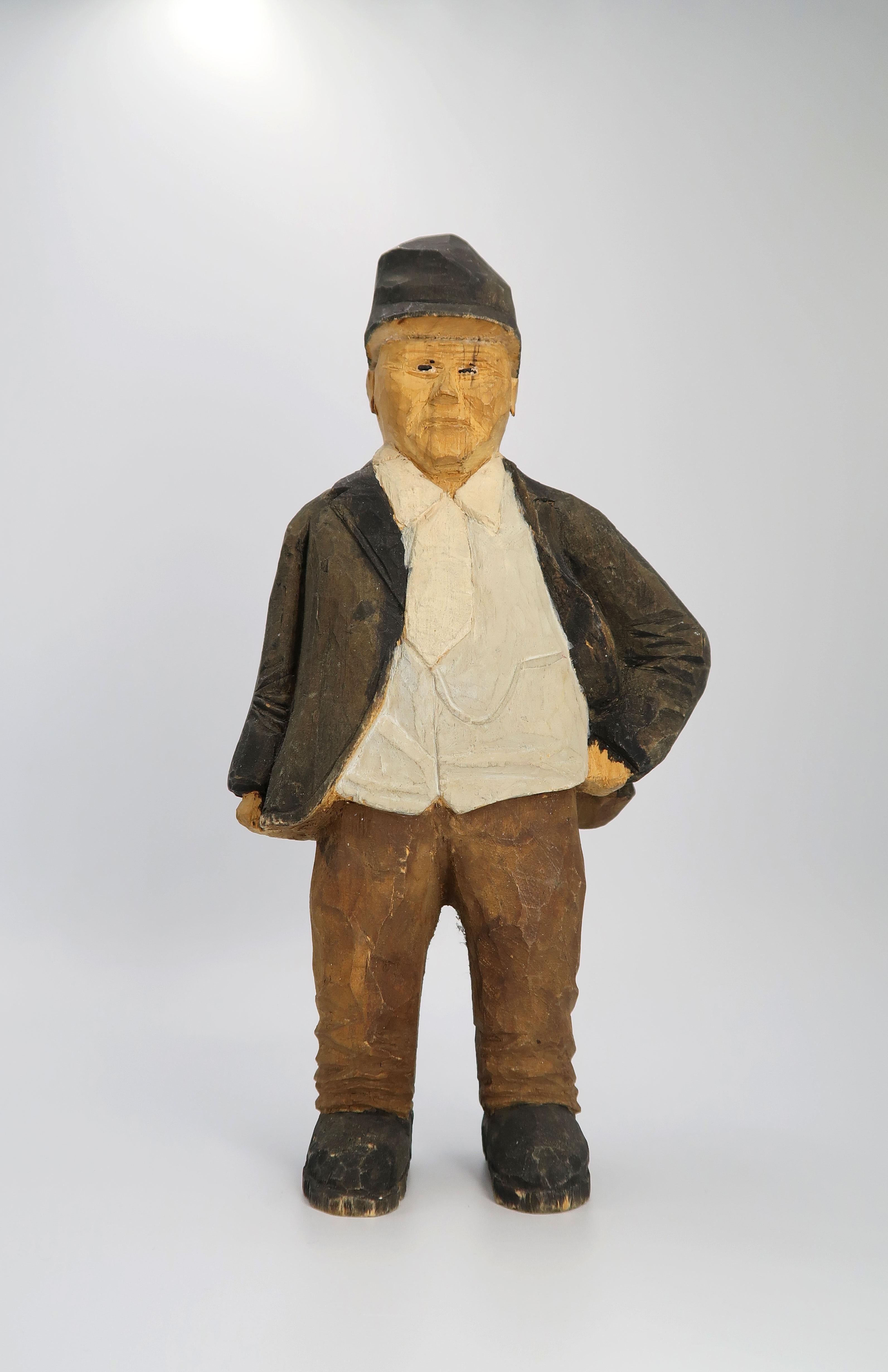 Expressive, rustic Swedish folklore midcentury wooden decorative sculpture of an older man in a traditional Swedish outfit. He stands leaning on one leg with a hand in one side as if waiting, and wears a white shirt, dark jacket, brown pants and a
