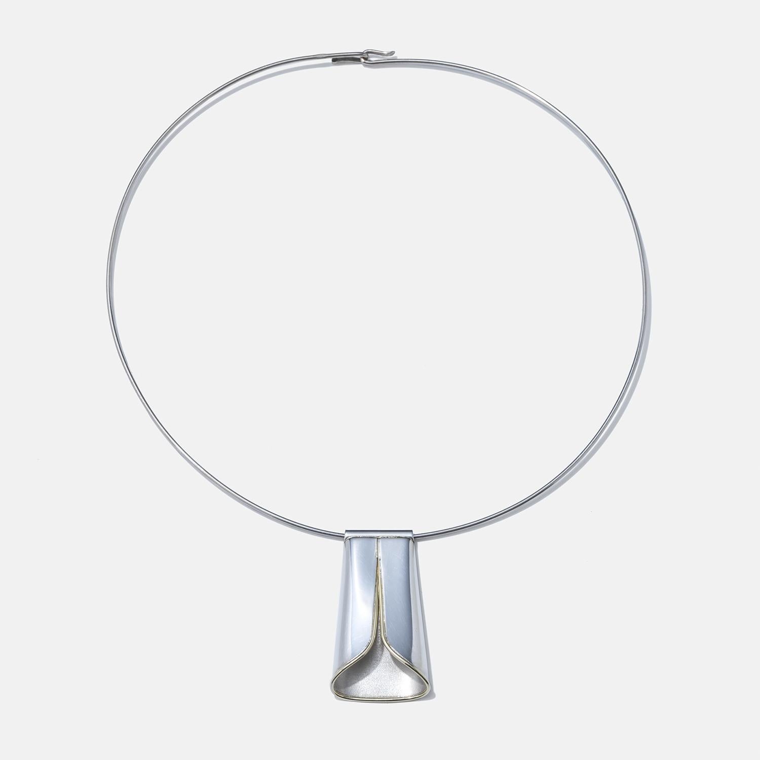 This is a sleek silver neck ring that opens at the back, making it easy to slip on and off. The pendant has a modern, broad V shape with a smooth silver finish and striking 18 karat gold edges that highlight its contours. The neck ring clasps