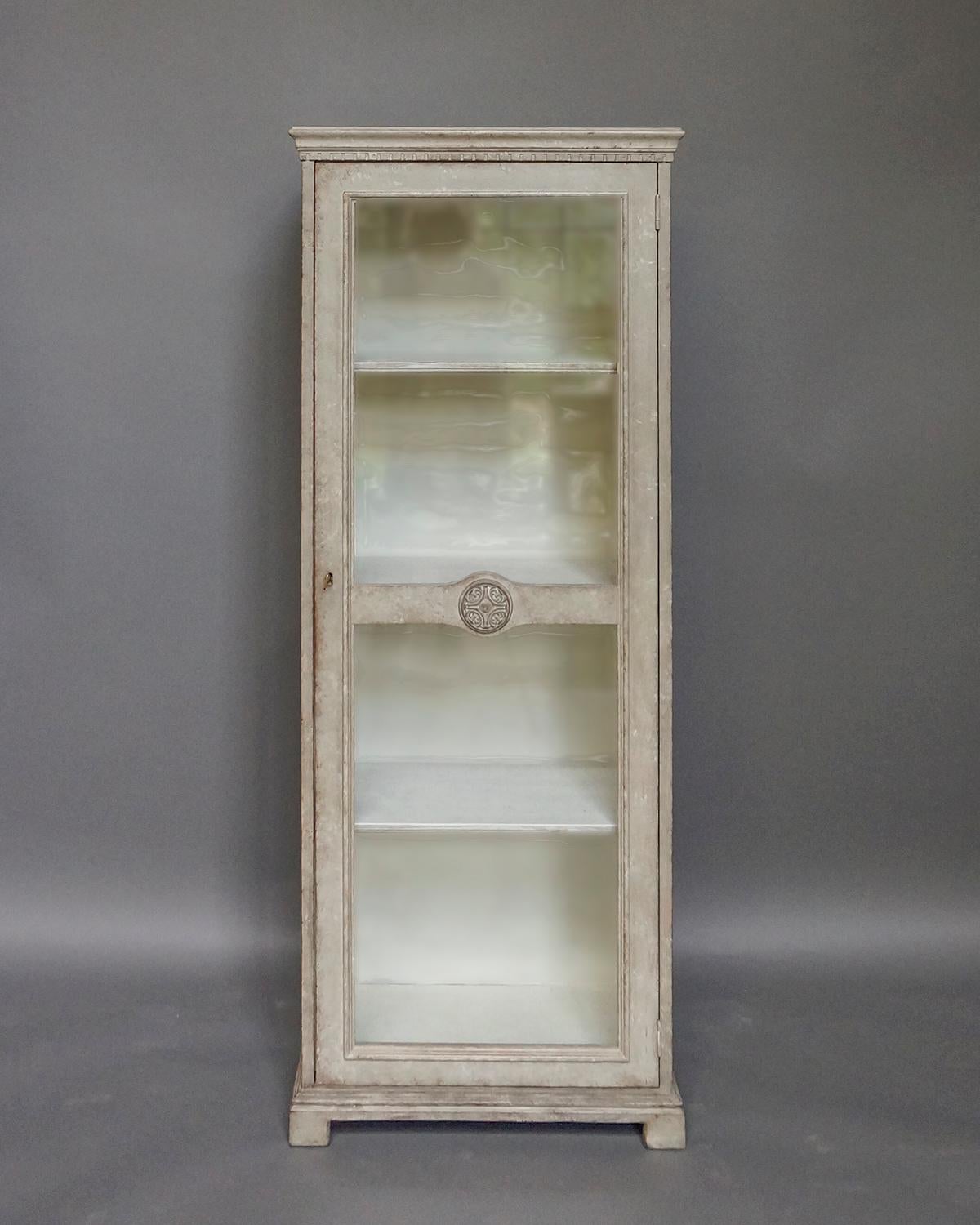 Gustavian Style Vitrine, Sweden, circa 1910. The single door has two glass panels separated by a horizontal member with a beautifully carved roundel. Shaped cornice with dentil molding and simple bracket base. Three internal shelves.