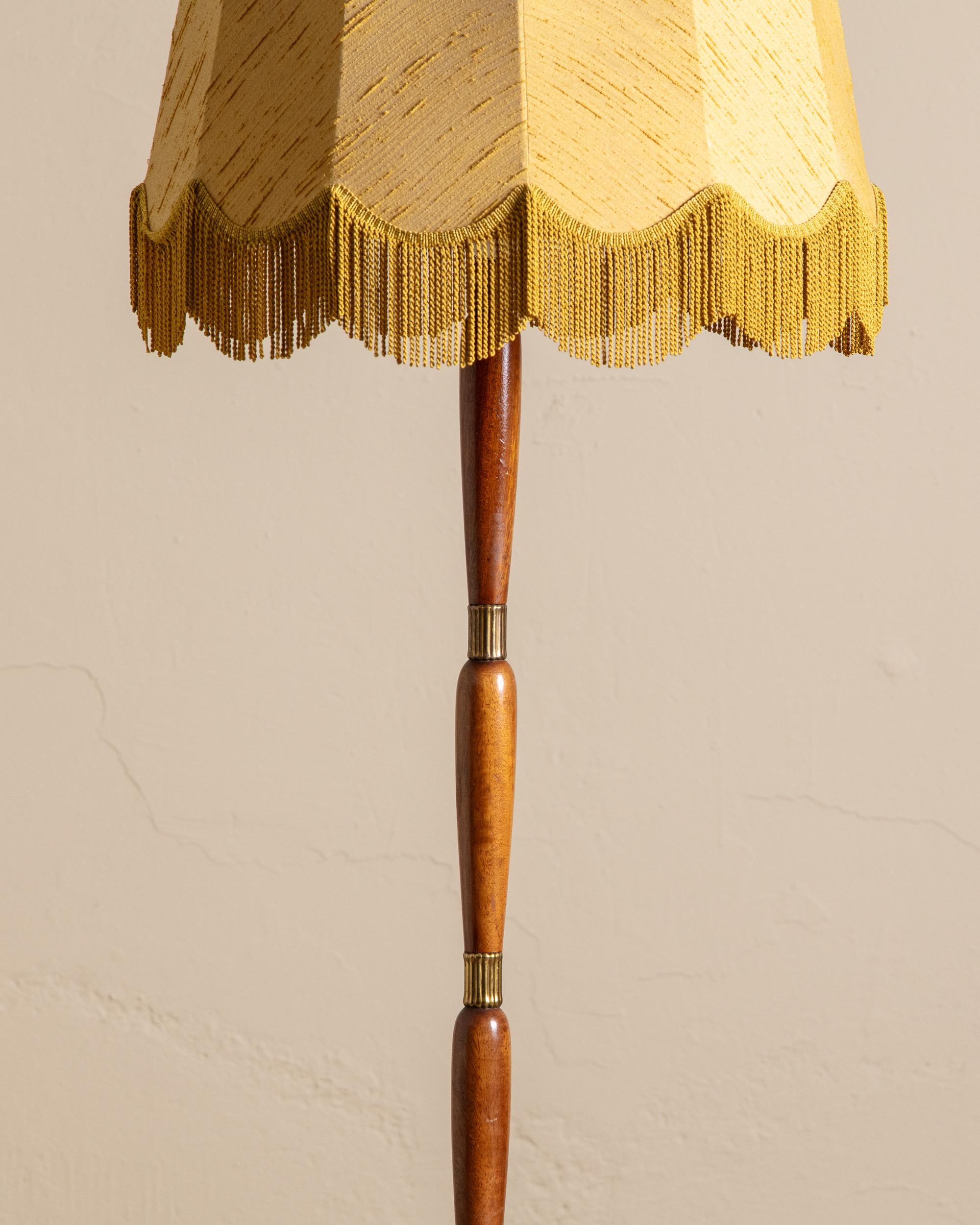 Un lampadaire vintage saisissant qui associe une forme sculpturale à des matériaux riches. La base en bois tourné présente des variations de tons chauds et est rehaussée d'élégants détails en laiton, offrant un contraste raffiné avec le grain