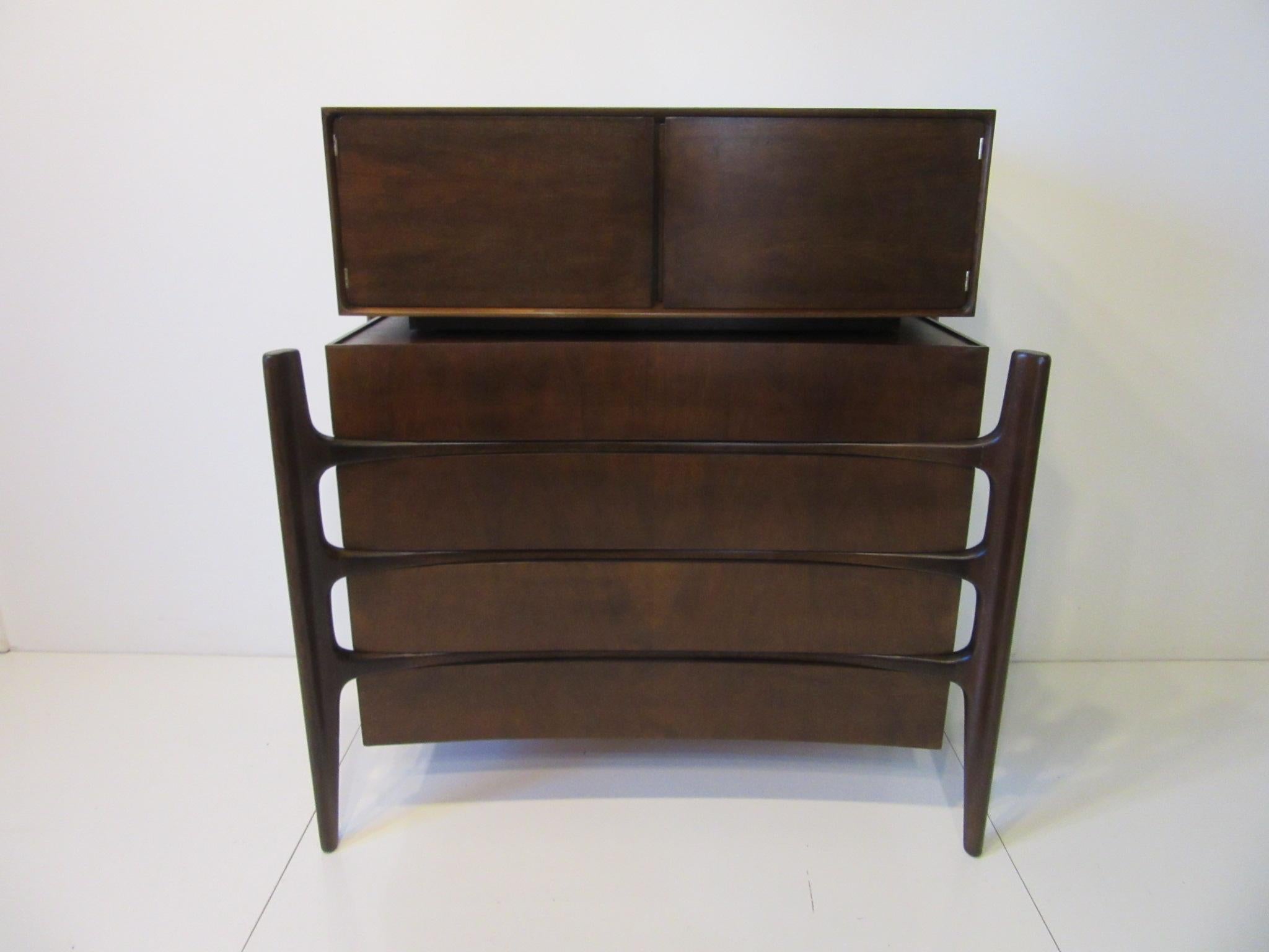 A well crafted 2-piece sculptural dresser / chest in a medium dark walnut finish with four drawer lower chest and upper two-door storage area having three sections. The interior is done in a clear birch wood to the inside drawers and storage