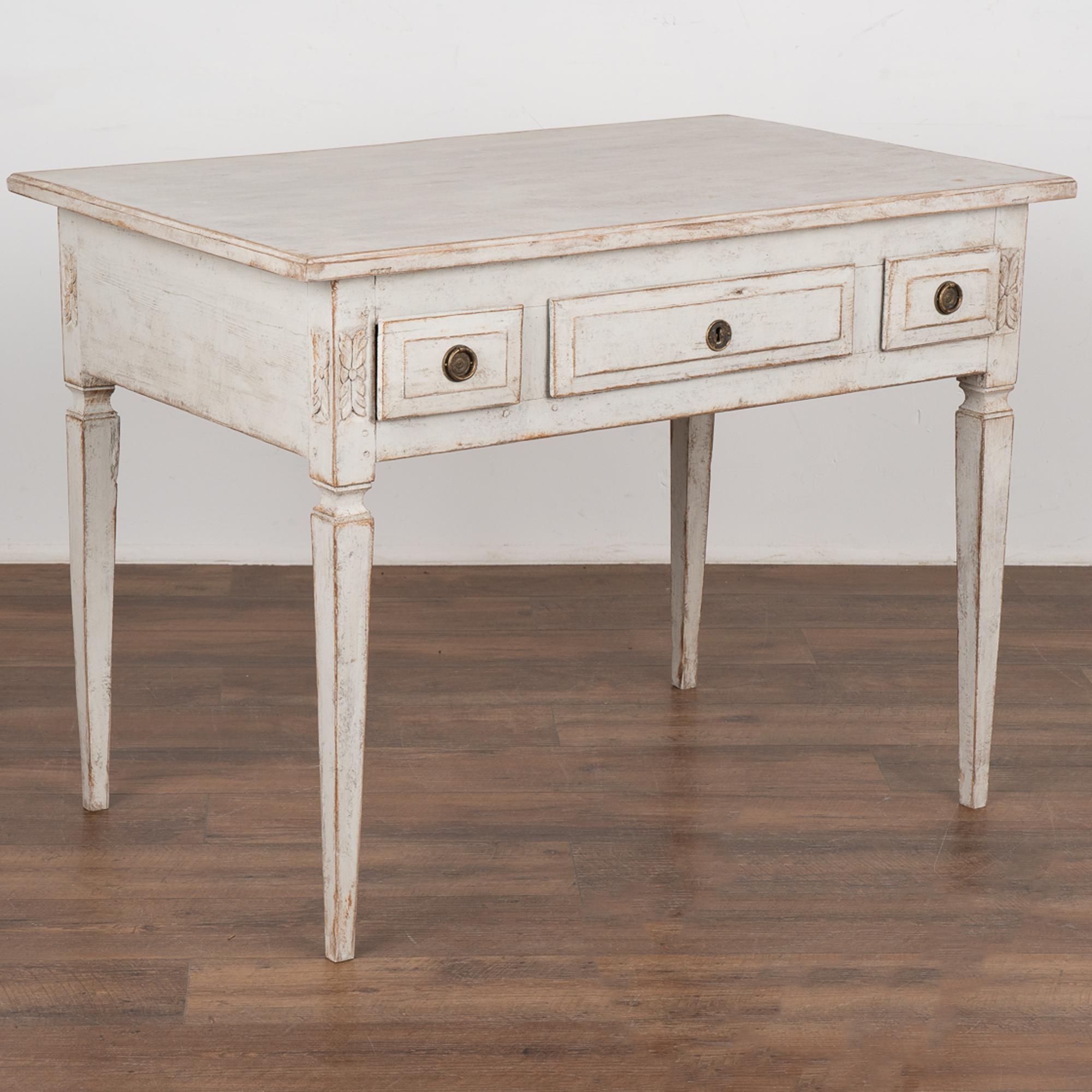 Swedish Gustavian pine side table with three drawers and lovely tapered legs.
Restored, later professionally painted in layered shades of white. 
Drawers function, outer two have brass pulls, skeleton key will be included as a 
