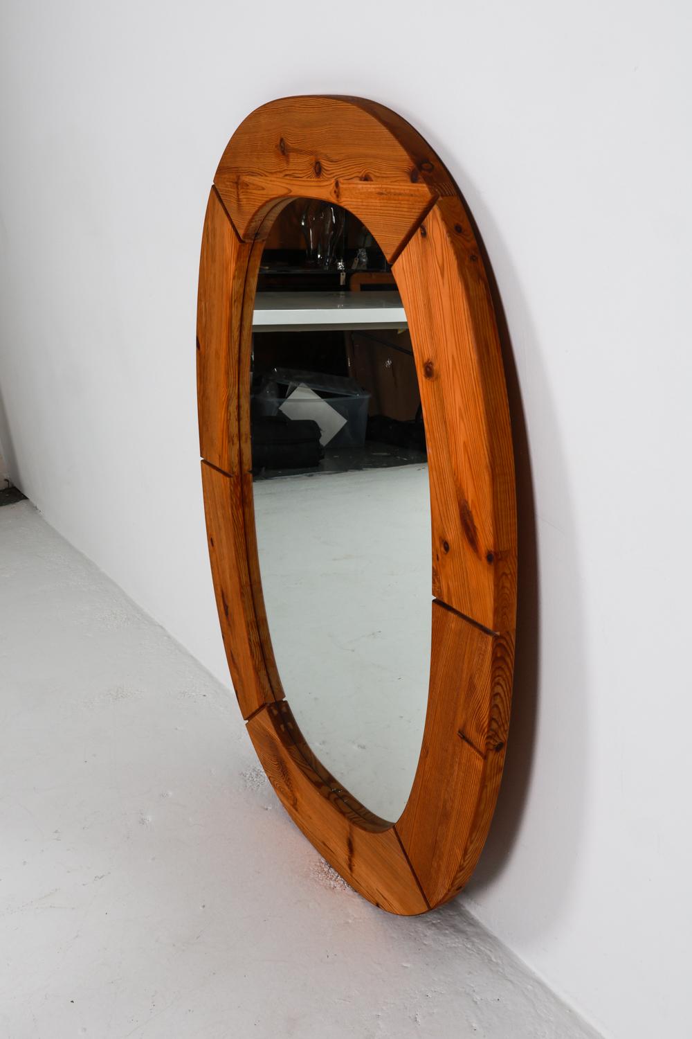 Ce miroir mural de taille impressionnante a été fabriqué en bois de pin massif pour son cadre de forme ovale. Les nœuds prononcés du bois et le grain du bois en relief confèrent une grande texture et un grand intérêt à la pièce. Le choix du pin pour