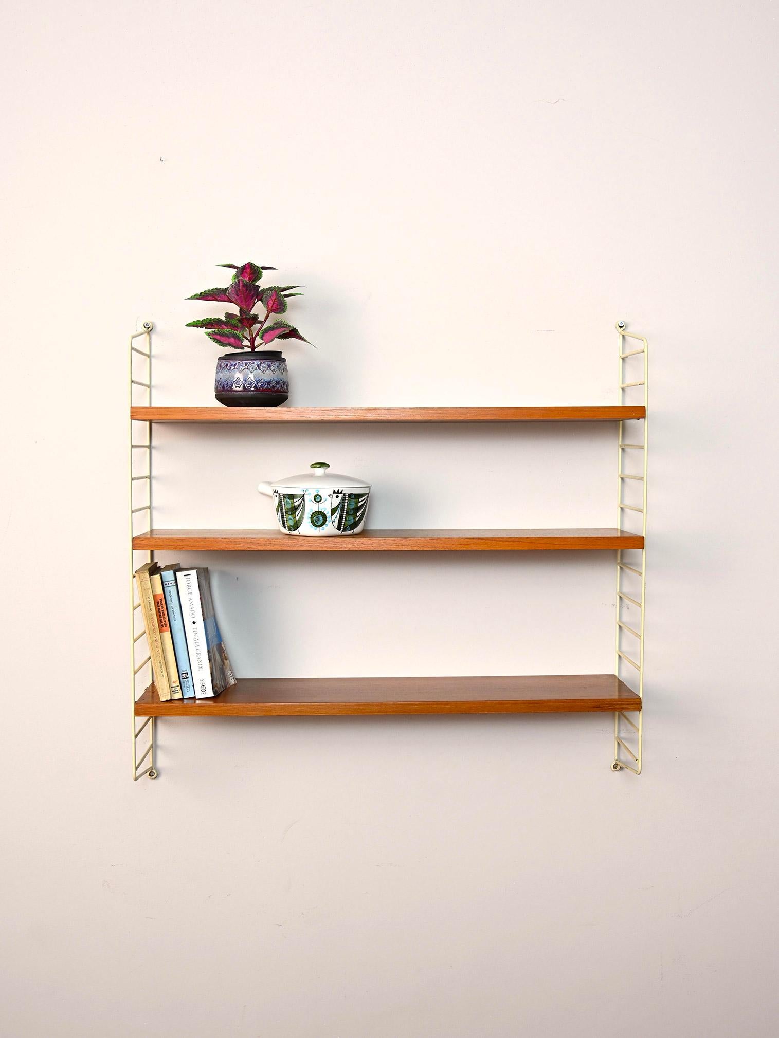 Original 1960s wall bookcase.

This simple shelving system consists of a coated metal side frame to which three teak shelves fit.
Simple and functional it can be hung in different rooms of the house.

Good condition. It has been restored with