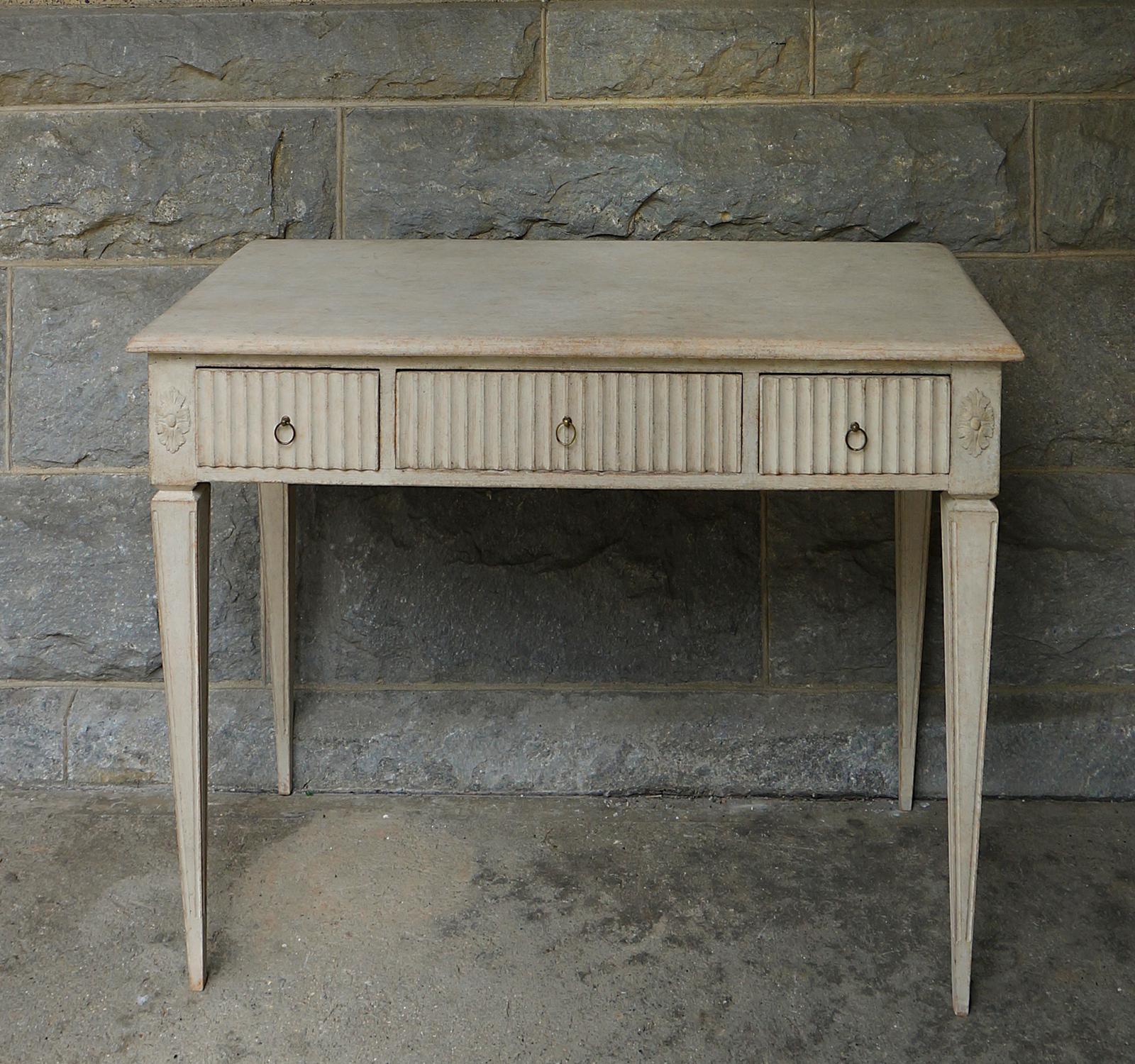 Gustavian style writing desk, Sweden circa 1880, with three apron drawers with vertical reeding and simple brass pulls. Applied rosettes at the corners above tapering square legs with incised detail. Nice roomy top perfect for a laptop computer or