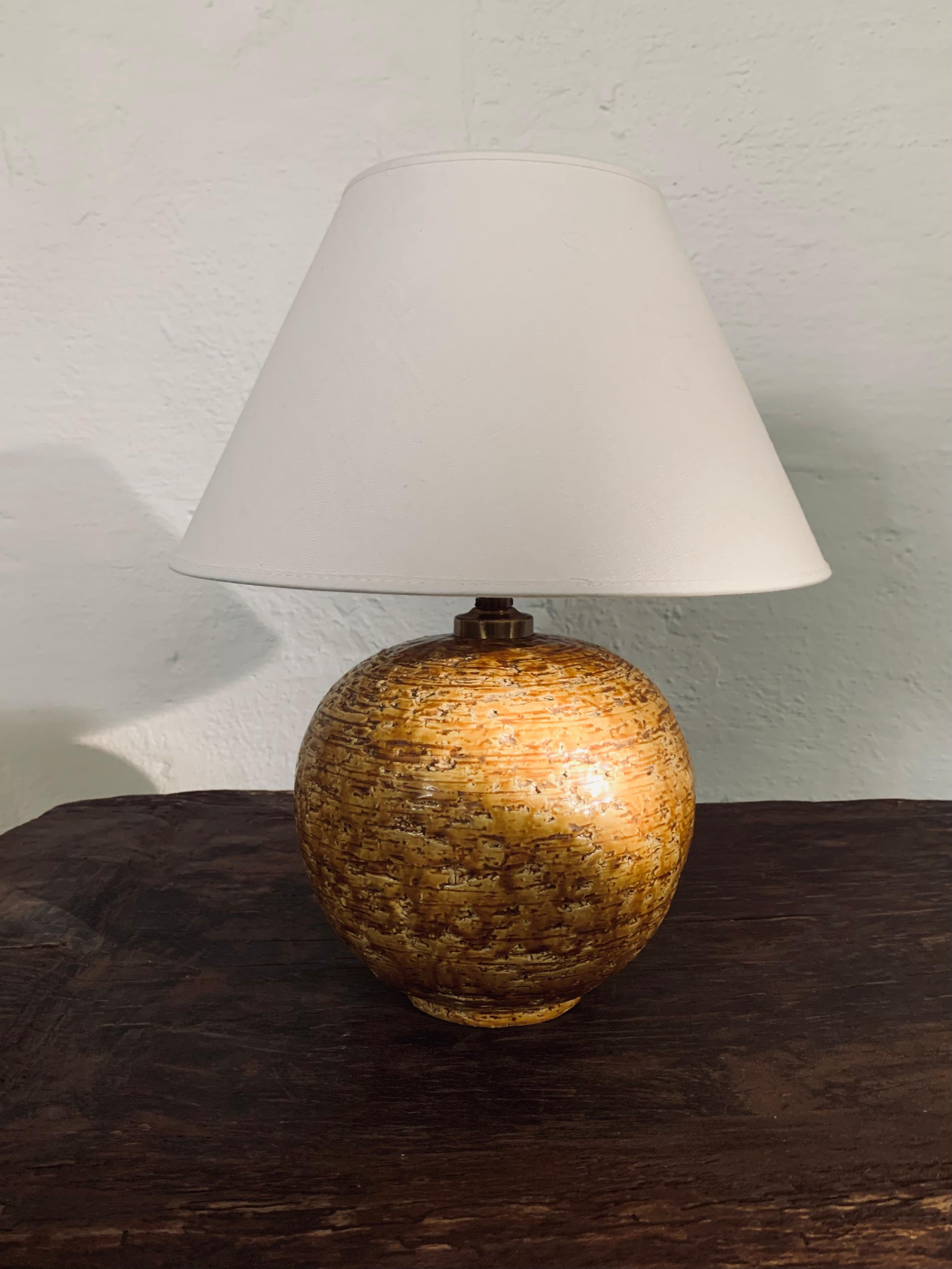 This stunning sculptural chamotte stoneware table lamp was designed by Gunnar Nylund for Rörstrand, Sweden, ca 1940s. Its spherical base has a tactile textured surface and mustard yellow glaze and comes with a white linnen shade. The lamp has been