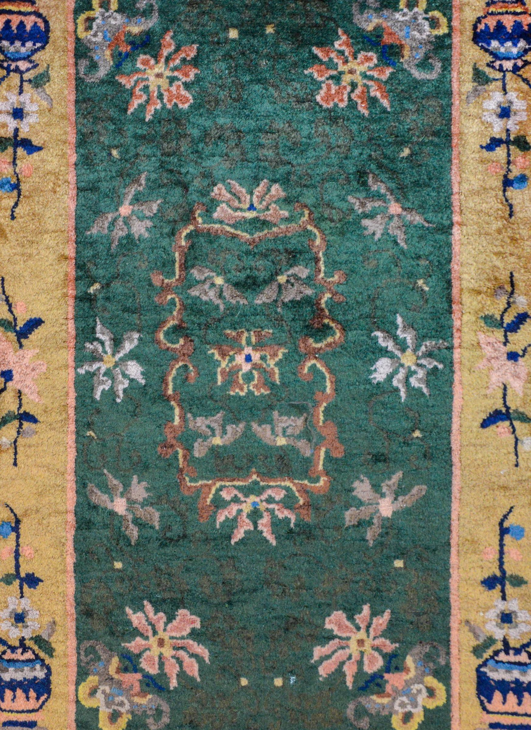 A sweet early 20th century Chinese Art Deco rug with beautiful pattern containing myriad chrysanthemums and lotus blossoms on a dark green background surrounded by a wide border containing scattered flowers and vines and a large potted peony in each