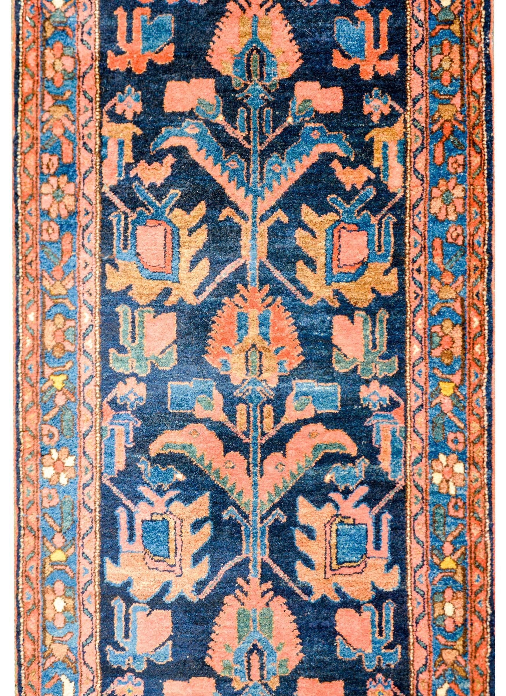 A beautiful early 20th century Persian Lilihan runner with an unusual pattern containing a vertically oriented floral pattern running the length of the rug woven in light indigo, green, pink, and orange on a dark indigo background. The border is