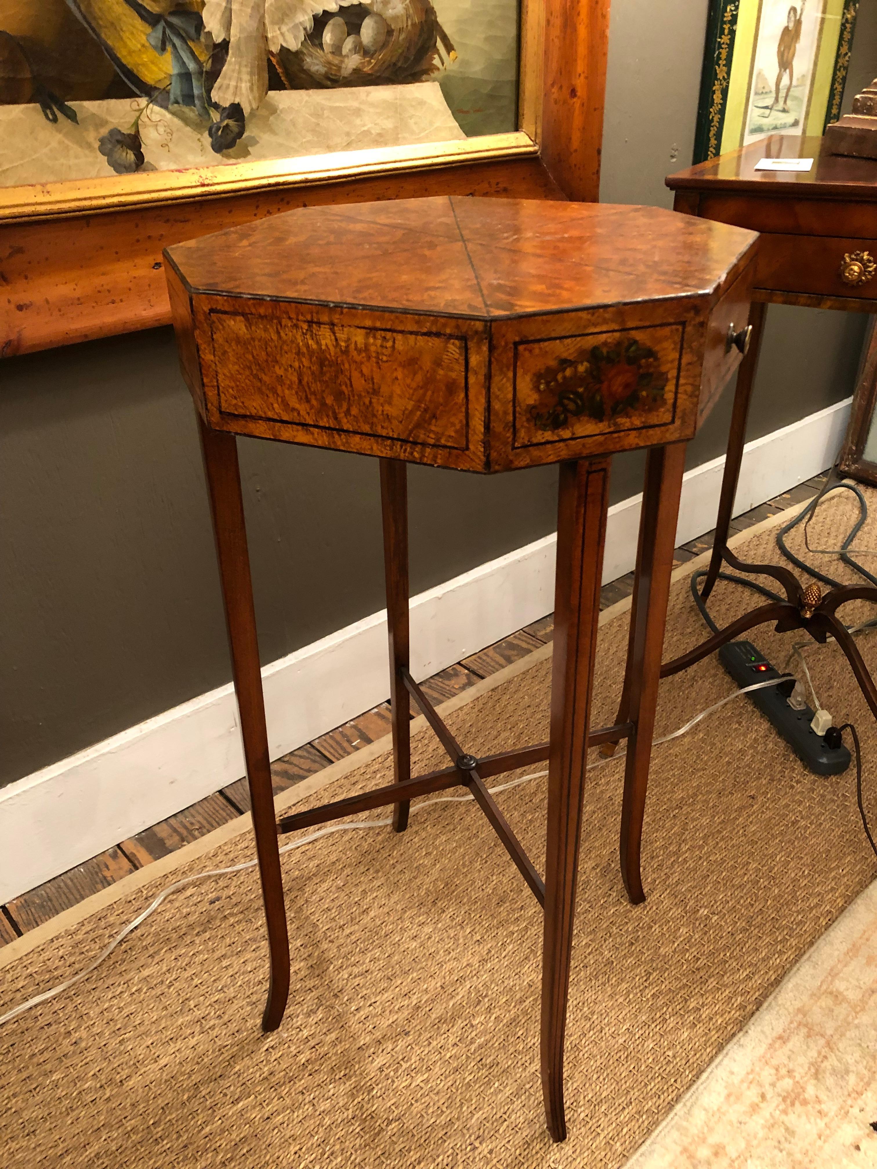 Lovely delicate side or end table having octagonal shaped top, single drawer, thin elegant legs and stretcher, and paint decorated to look like burl wood with beautiful floral decoration on side.