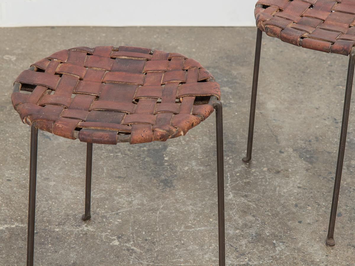 Rare cognac leather and iron stools designed by Lila Swift and Donald Monell. The seat is made of woven leather straps and secured with cord and iron ring on the underside. Minimal wrought-iron tripod base is sturdy and strong. Nice age to the
