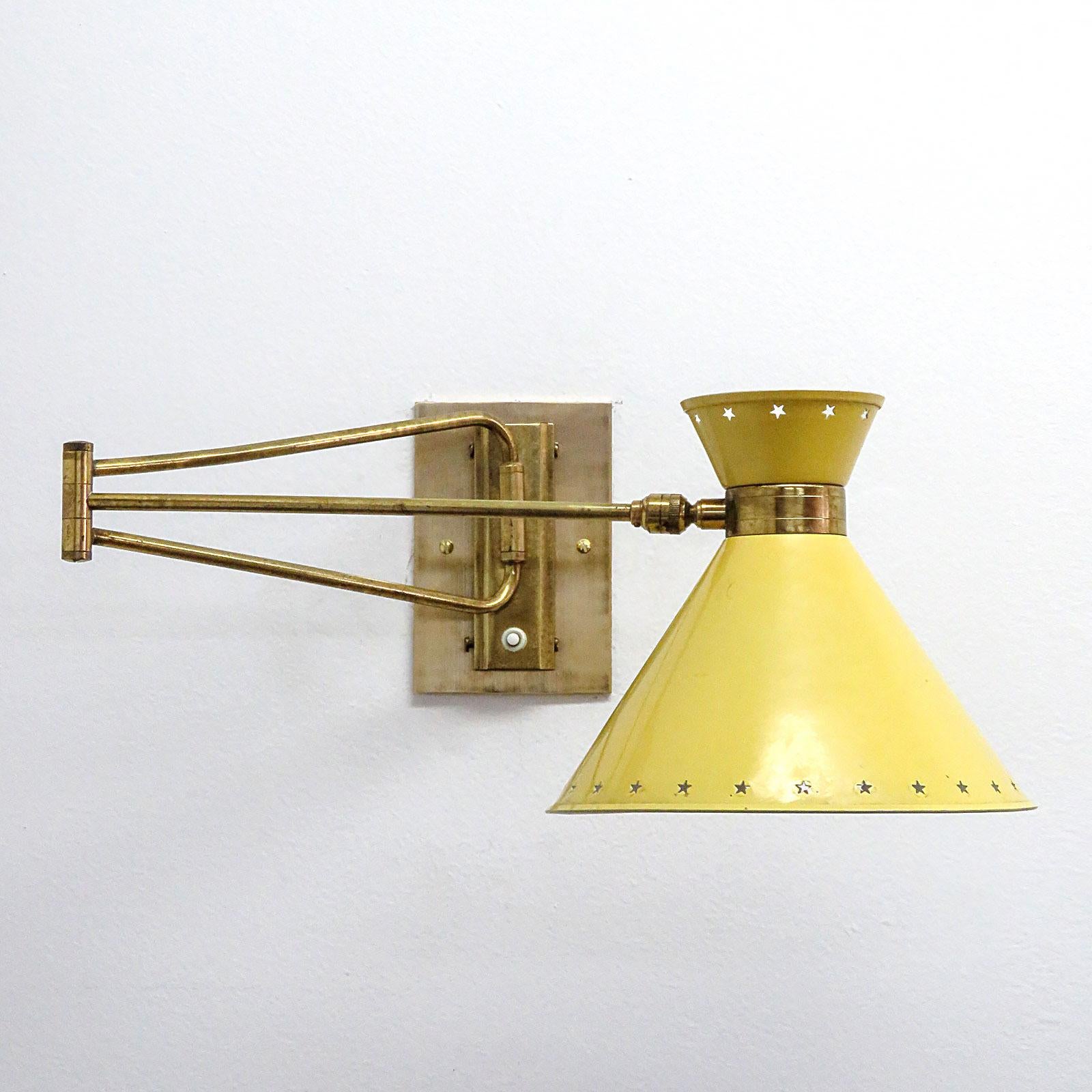 Wonderful double cone swing arm wall light by Rene Mathieu for Lunel, France 1950, original yellow colored enameled metal shade with decorative star perforations on an articulate brass arm and custom brass backplates, wired for US standards, one E12