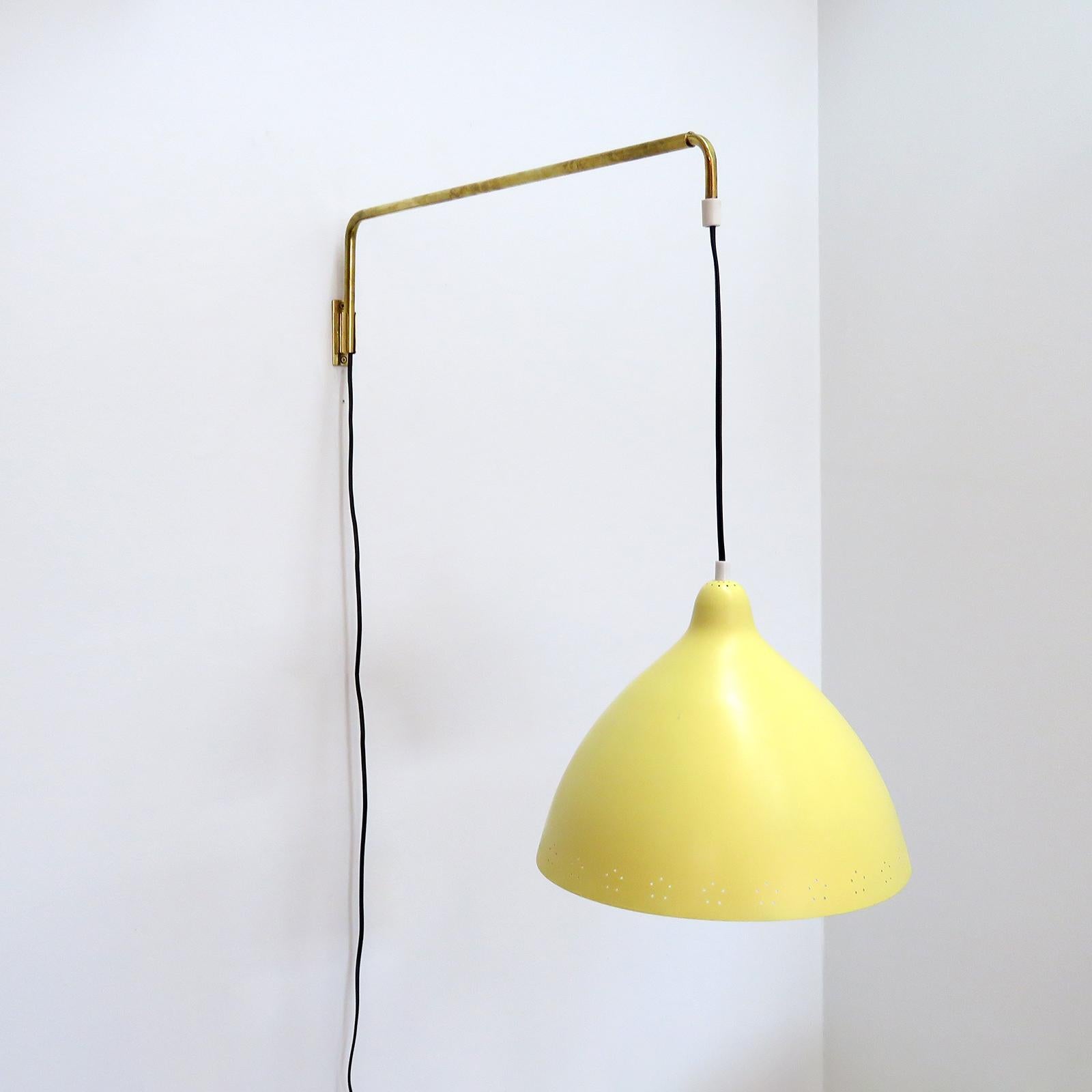 Wonderful swing arm wall lights by Lisa Johansson-Pape for Orno, Finland, 1960, shades in yellow painted metal with elegant perforations along the bottom rim of the shade, on a brass arm that can extend 36-56