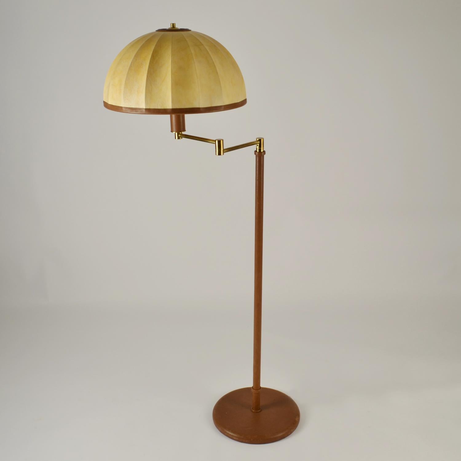 Lámpara de pie Swingarm de cuero de alta calidad de los años 60 con pantalla de cúpula apergaminada que crea una luz cálida. La pantalla de tambor hecha a mano en piel de pergamino se une con bordes de piel, unidos por elementos de latón a la base.