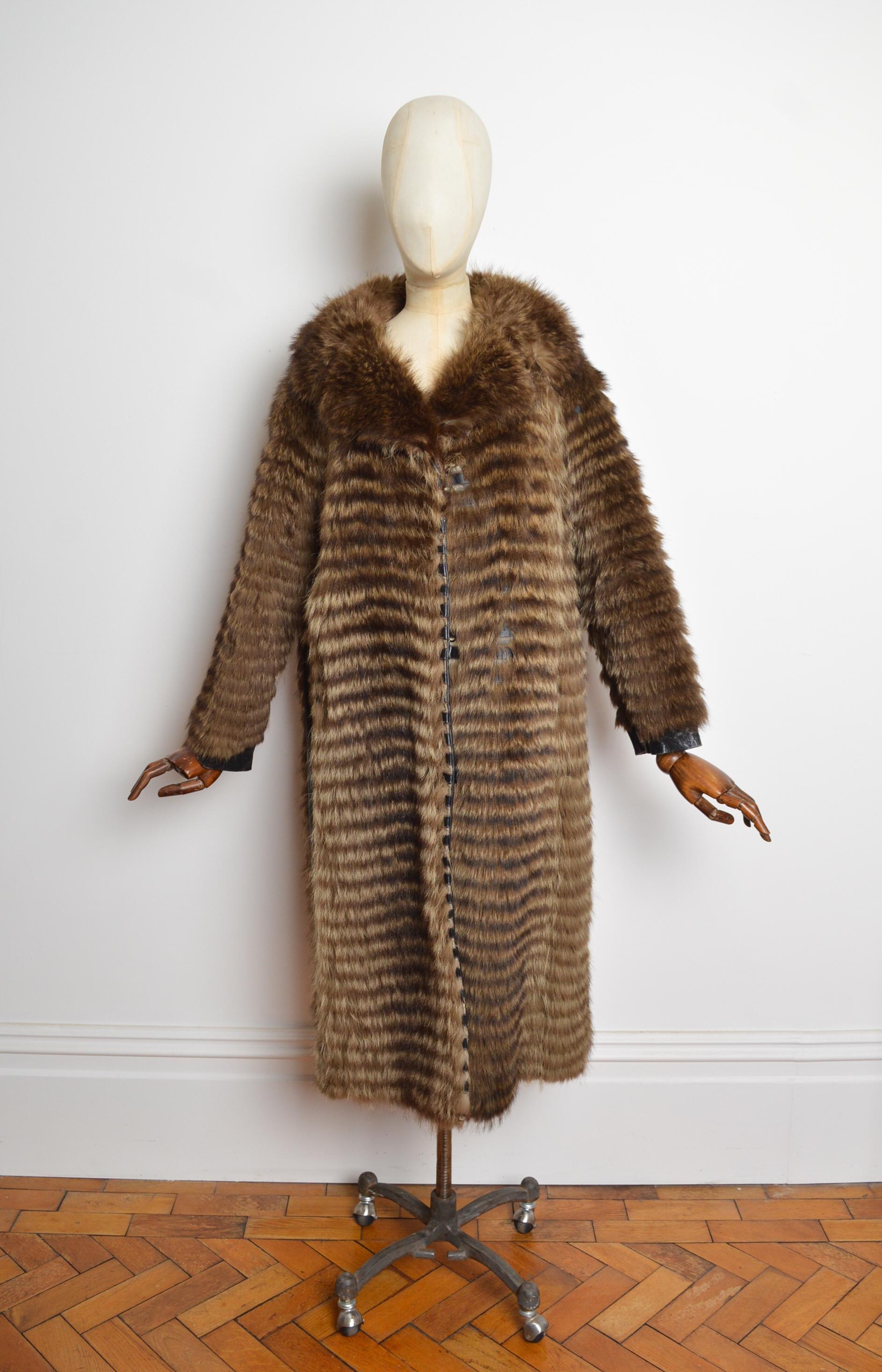 Manteau long en fourrure rayée vintage des années 1960 de la maison PIERRE CARDIN. Il est doté de manches longues, d'un col, de poches sur les hanches, d'empiècements en cuir et d'une doublure intérieure en satin rose Organdy. 
FABRIQUÉ EN