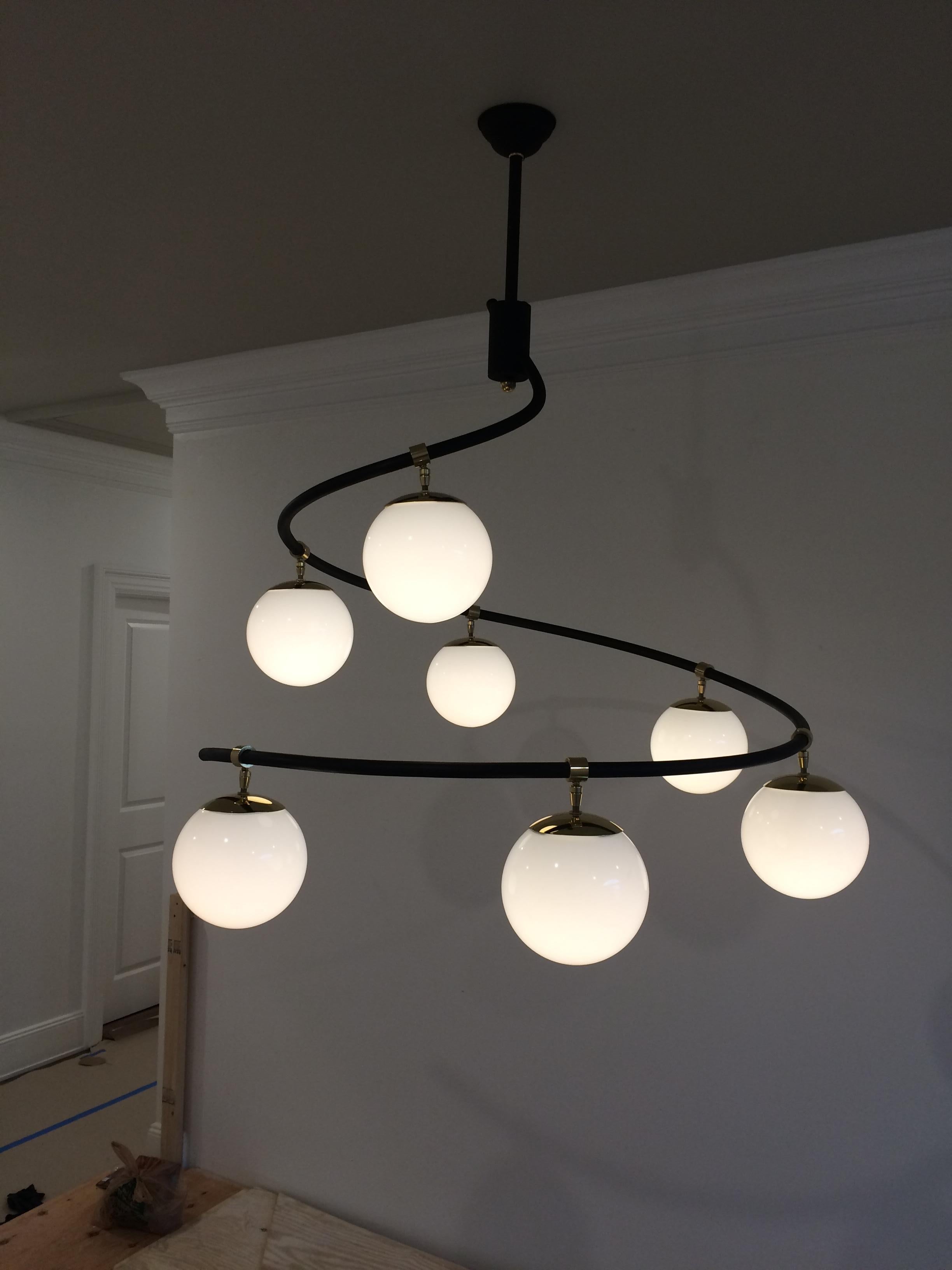 Curvaceous swirling seven-light chandelier with blackened tubular steel structure, solid brass fittings and 7 milk glass globes. Comes in two standard sizes, or custom made to your specifications.
Images also show the larger size Swirl, and also a