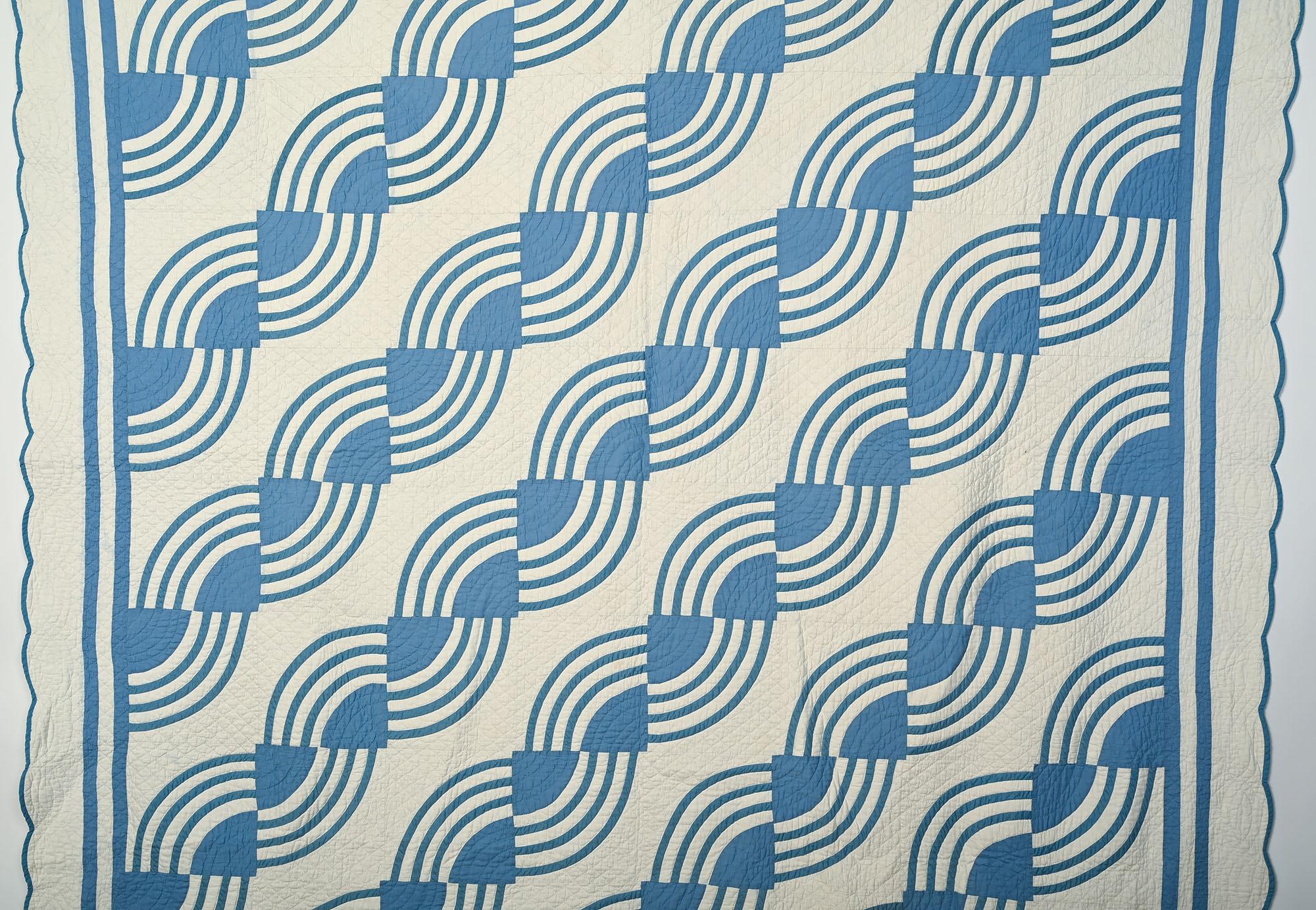 Anmutiges und ungewöhnliches Quiltmuster aus wirbelnden Fächern. Der Quilt ist in einem perfekten Blauton gehalten. Die weißen Flächen sind schön mit Rauten gequiltet und die blauen Blockmitten folgen der Kurve des Musters. Der weiße Rand ist mit