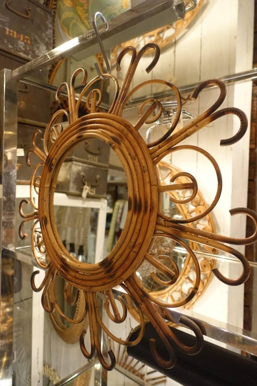 Magnifique et élégant miroir rétro en rotin, de France. Le cadre est formé pour représenter le soleil avec des rayons courbes tourbillonnants. Verre de miroir rond d'origine. Tissé à la main au milieu du 20e siècle. Super décoratif et parfaitement