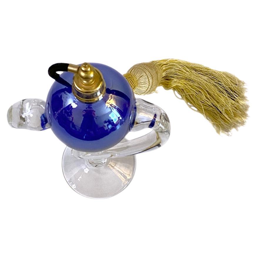 Il s'agit d'un flacon de parfum à piédestal tourbillonnant avec atomiseur. Le corps du flacon de parfum boule en verre bleu colbalt est orné d'une couche d'aurore boréale et est soutenu par un piédestal en verre clair tourbillonnant. Il est livré