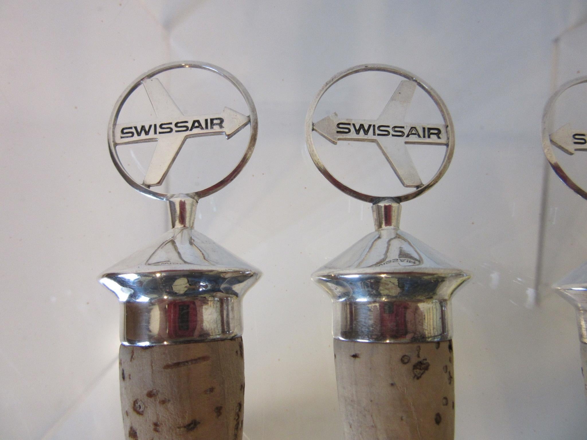 A set of four Swiss Air airlines logo wine / bottle stoppers with a jet plane form and Swiss Air in black on both sides having a silver cast topper and cork bottom. From the 1970s and in original vintage condition the perfect way to class up the bar